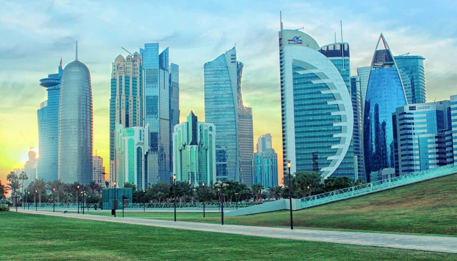 Qatar 桌布 壁紙 — 日落時分充滿活力的城市景觀，現代摩天大樓在柔和的藍天下反射出金色光芒。