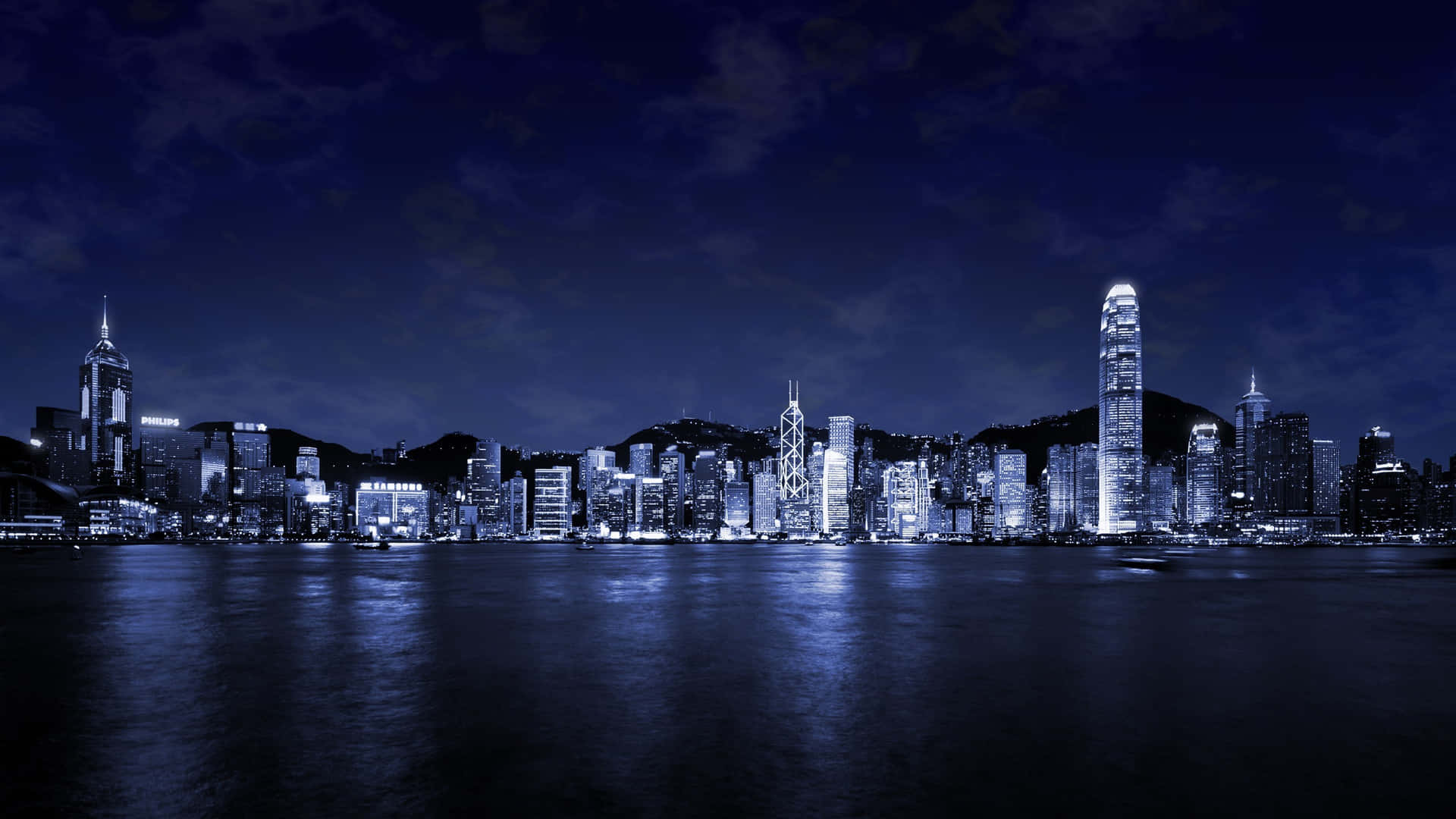 日落時分壯麗的城市天際線景觀 壁紙 — 令人驚嘆的單色香港夜景，摩天大樓在深藍色天空下閃爍，倒映在平靜的水面上。