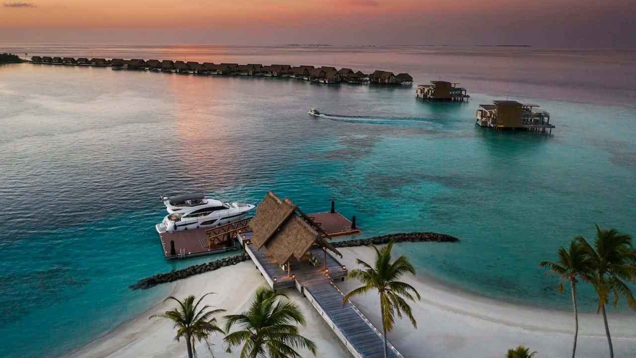 Maldives Island 桌布 壁紙 — 日落時分熱帶島嶼上豪華水上平房和遊艇停泊的鳥瞰圖。
