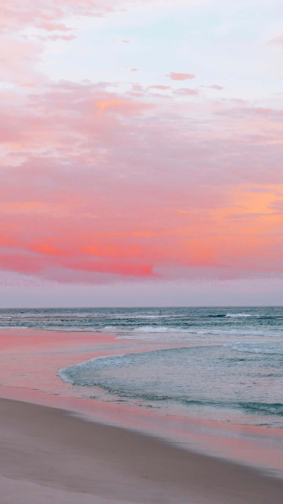 Pink Beach 桌布 壁紙 — 日落時分的寧靜海灘，柔和的粉紅色和橙色雲彩倒映在平靜的海浪和濕沙上。