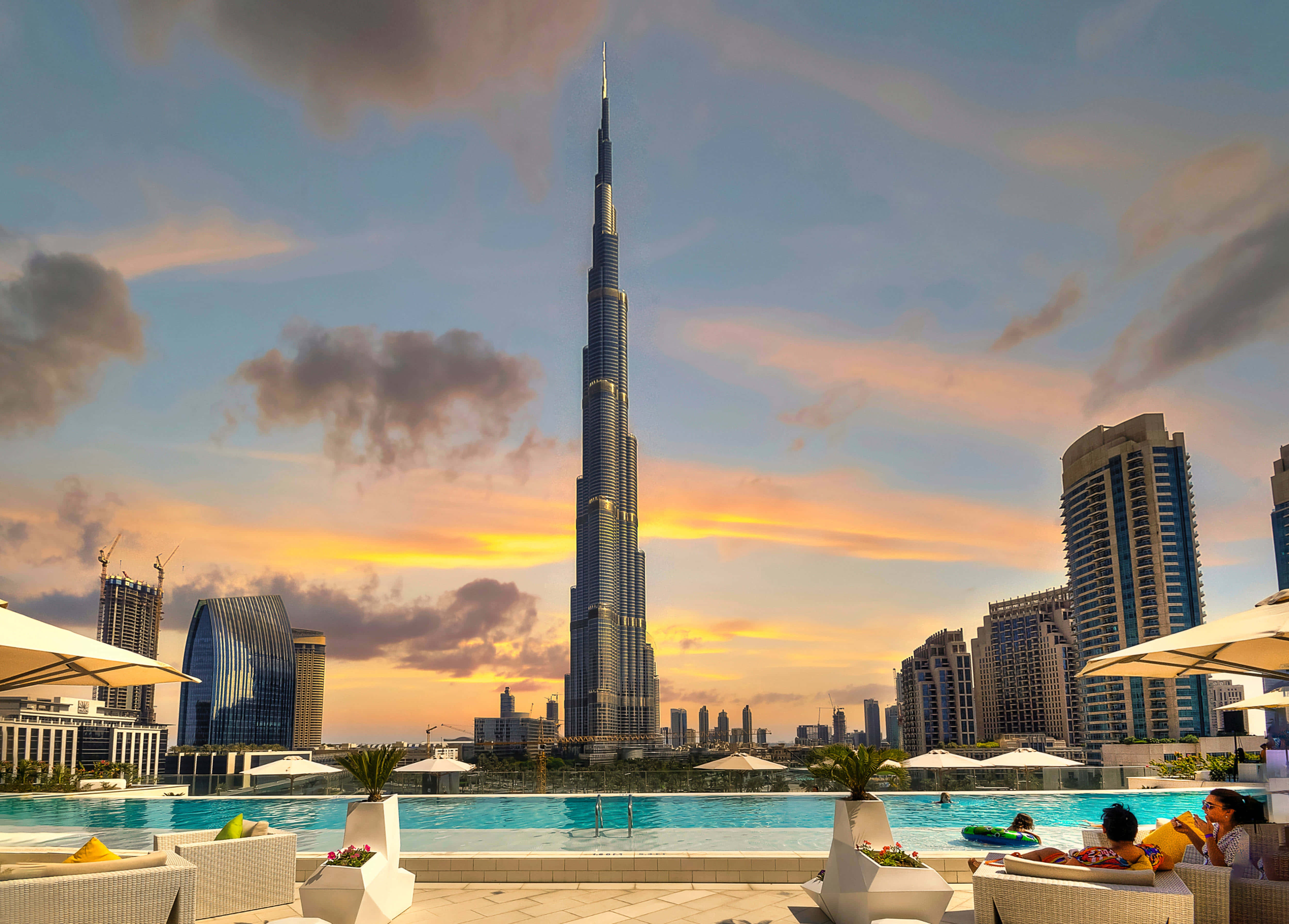 Burj Khalifa 桌布 壁紙 — 日落時分的屋頂泳池，哈利法塔高聳於杜拜天際線之上，客人在遮陽傘下放鬆。