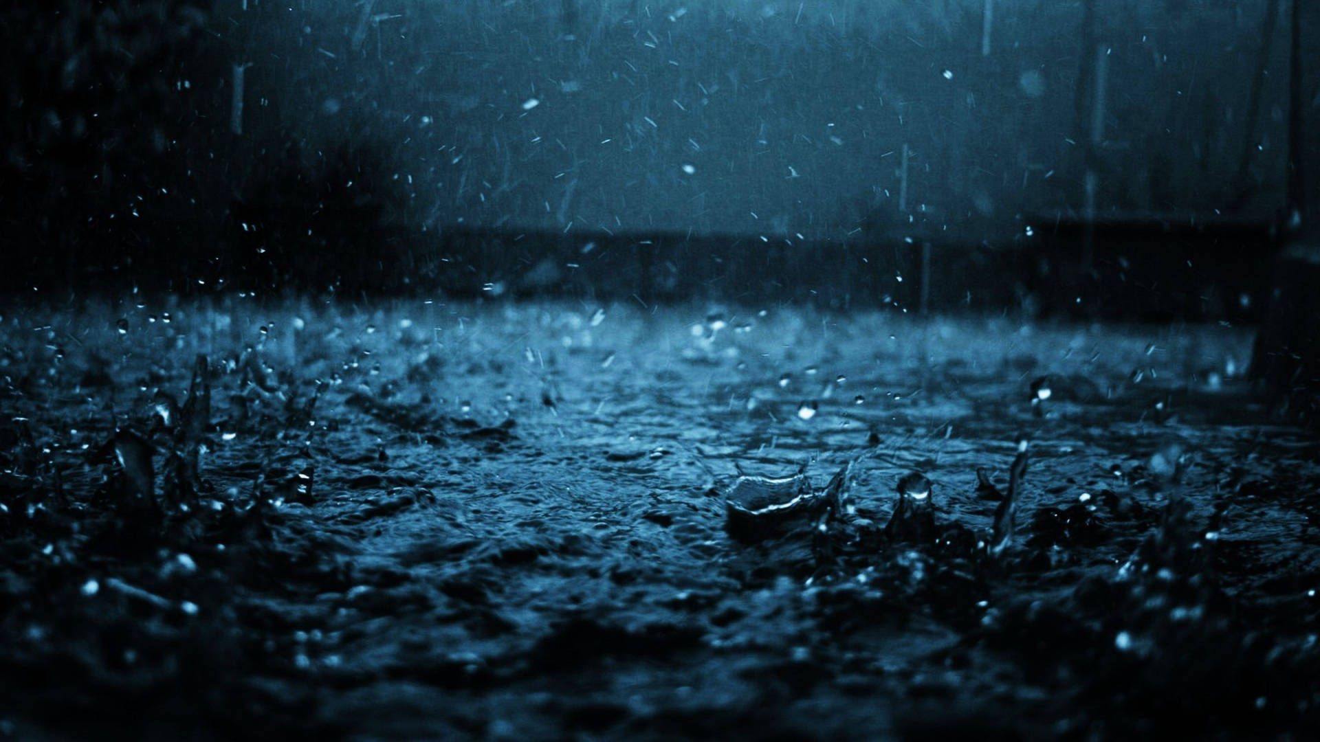 雨滴在深藍色夜空下飛濺在潮濕的地面上。