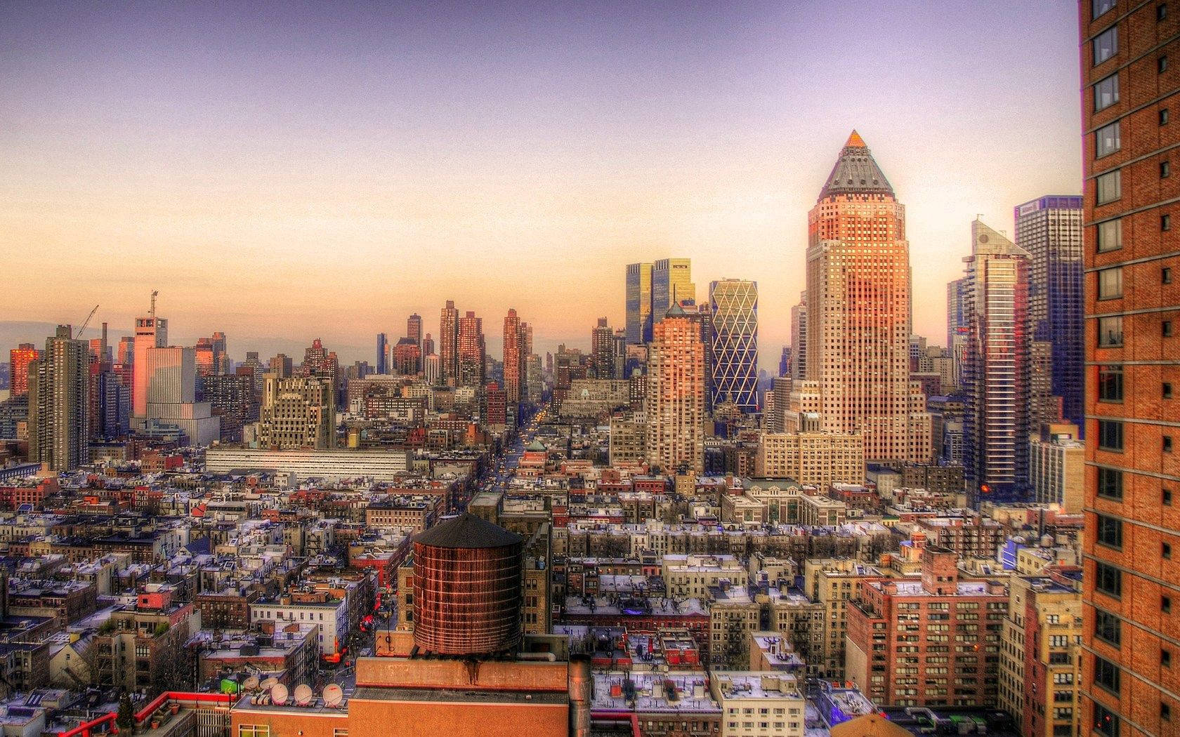 日落時分的紐約市美景 壁紙 — 夕陽西下，溫暖的金色和紫色色調籠罩著密集的城市天際線，摩天大樓刺穿逐漸消失的天空。