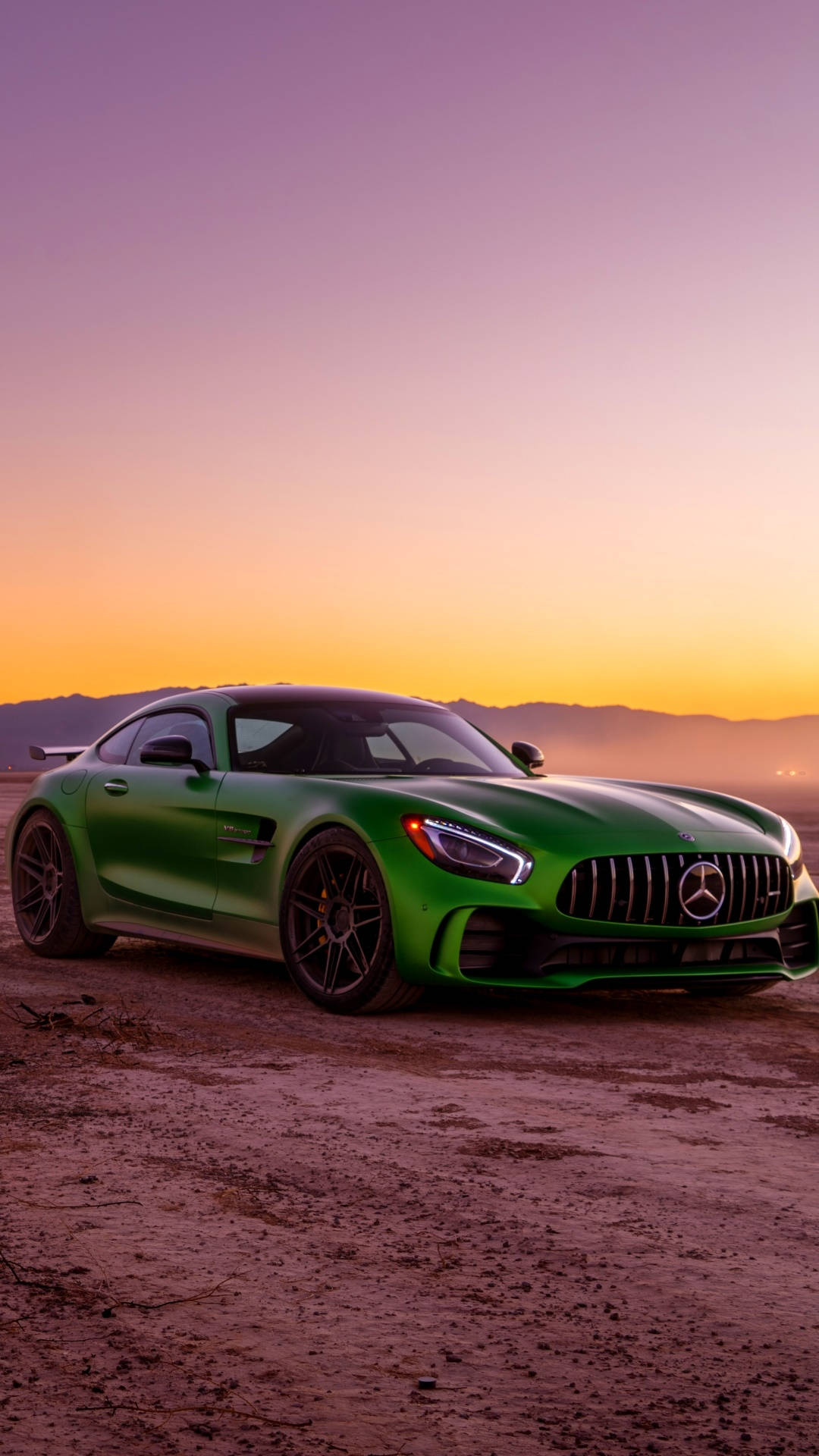日落時分的綠色AMG 壁紙 — 一輛充滿活力的綠色Mercedes-AMG GT停泊在塵土飛揚的地形上，背景是漸變的日落天空和遠處的山脈。