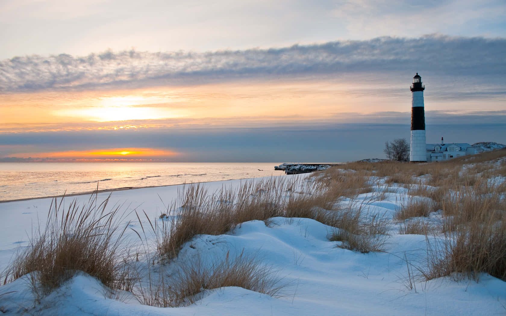 Winter Beach 桌布 壁紙 — 日落時分的雪灘，一座黑白燈塔高聳在金色天空下。