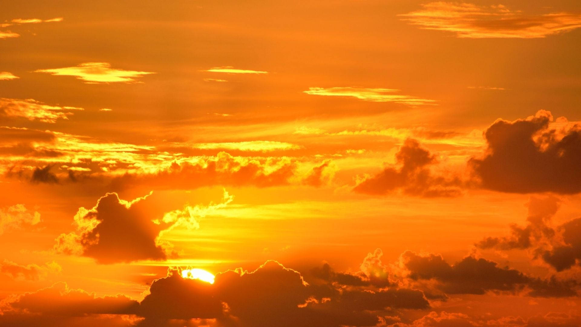 夕陽天空，橙色雲朵，雲後發光的太陽