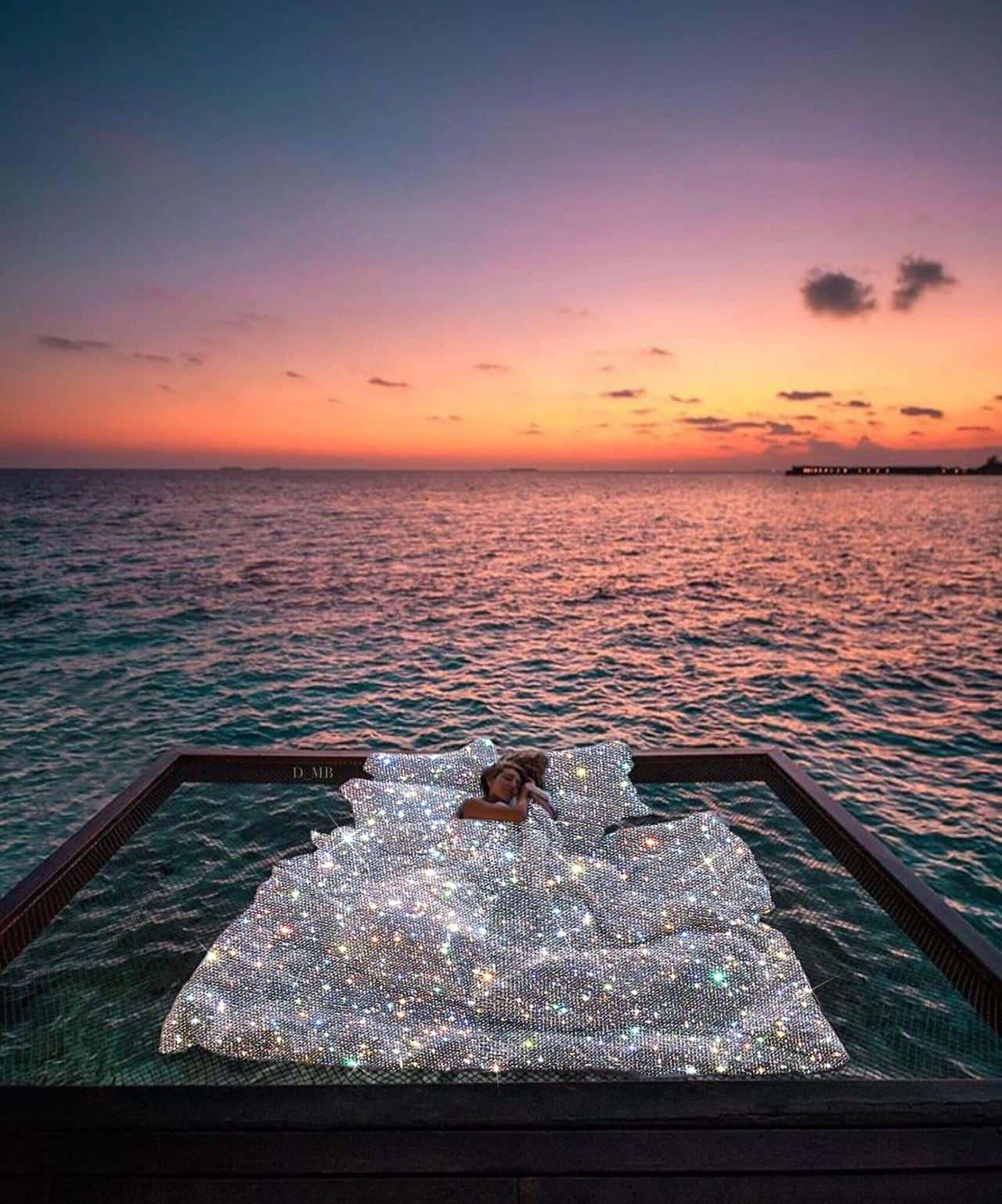 日落海中漂浮的床美學圖 壁紙 — 一個人在日落時分躺在漂浮在海面上的閃爍床上，天空呈現鮮豔的橙色和紫色。
