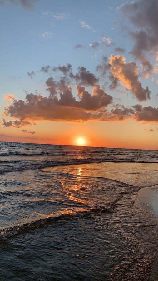 日落海灘美麗雲朵圖 壁紙 — 夕陽將天空染成橙色和粉紅色，海浪在散落的雲朵下輕輕拍打海岸。