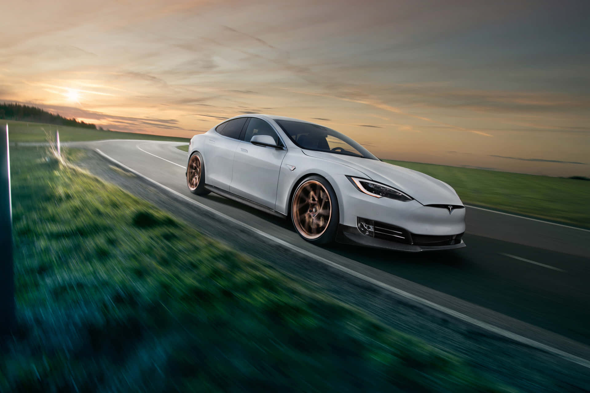 白色Tesla Model S在日落時分的鄉村道路上疾馳，背景是模糊的綠色田野。
