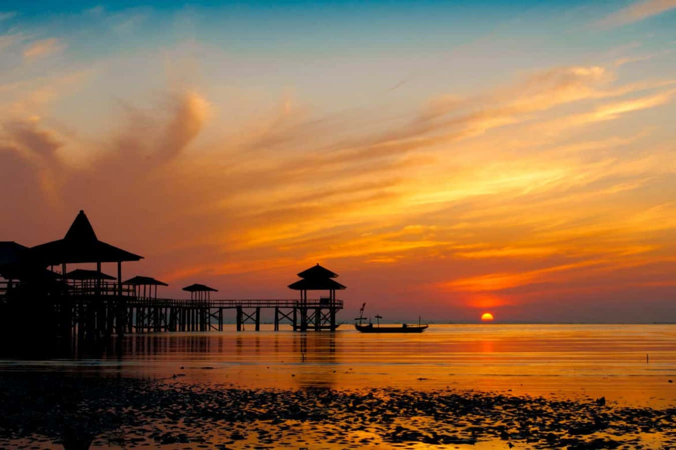 夕陽下平靜水面上碼頭和船隻的剪影，天空呈現鮮豔的橙色和粉紅色。