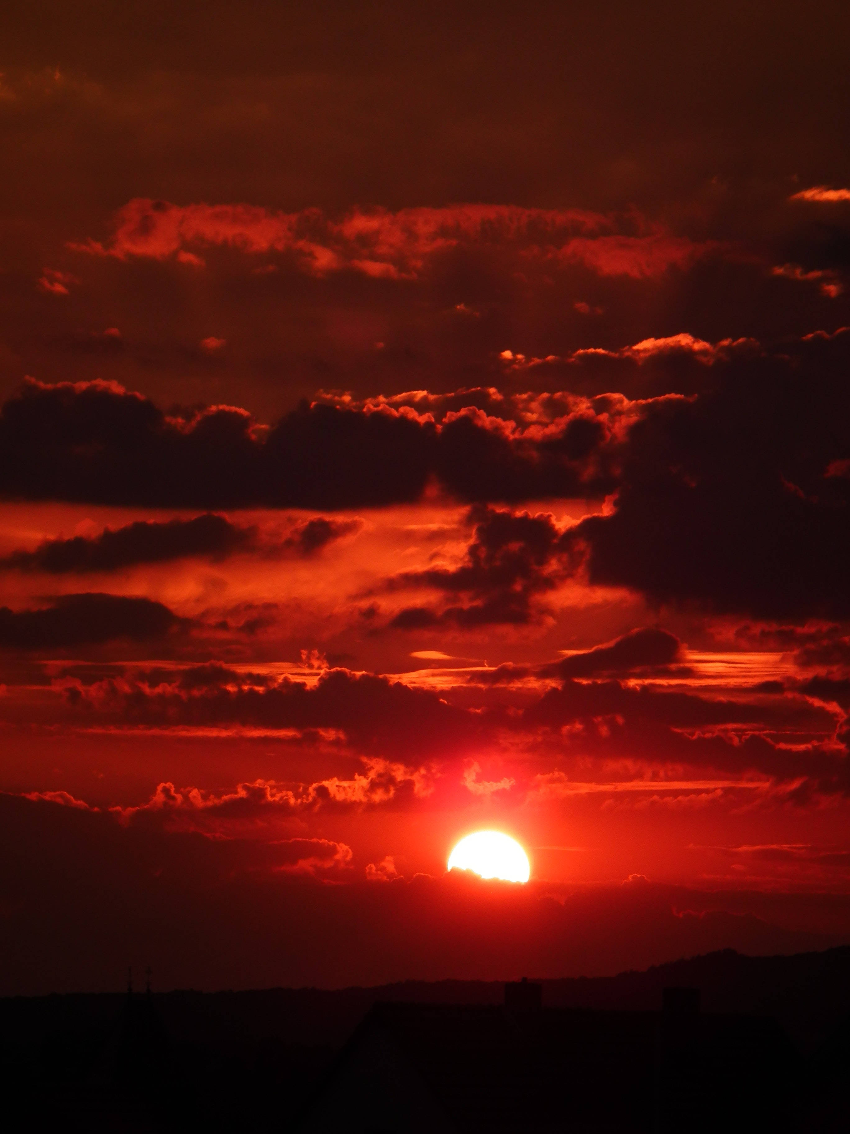 日落紅霞的唯美天空 壁紙 — 一輪火紅的太陽在烏雲後落下，為剪影般的地平線投下強烈的光芒。