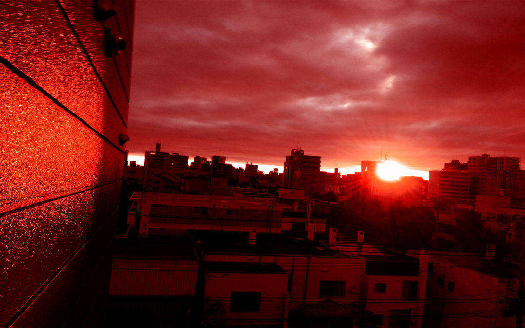 日落紅黑手機 壁紙 — 夕陽在建築物後方落下，城市景觀沐浴在強烈的紅光中，在紋理牆壁上投下長長的陰影和發光的倒影。
