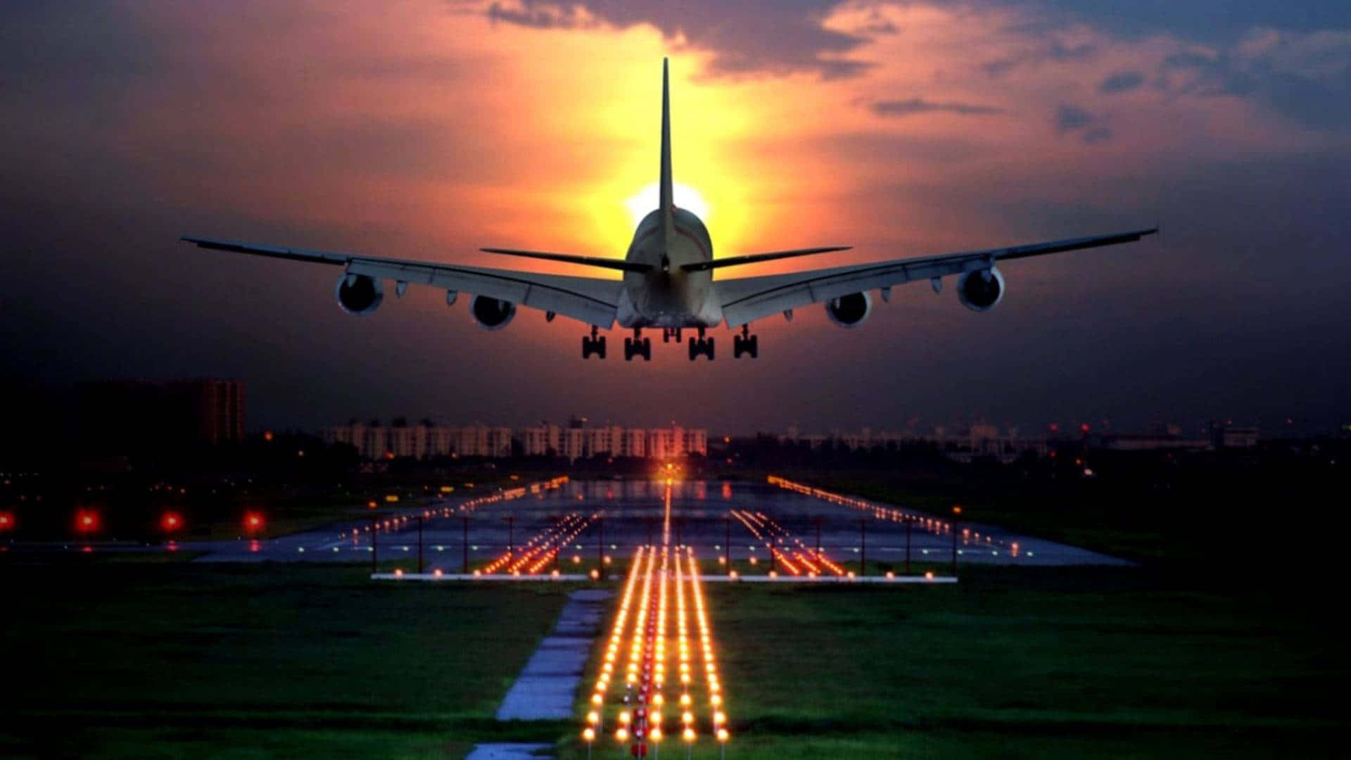 日落與飛機起飛背景 壁紙 — 一架大型飛機在金色夕陽光芒中降落到跑道，遠處的城市燈光閃爍。