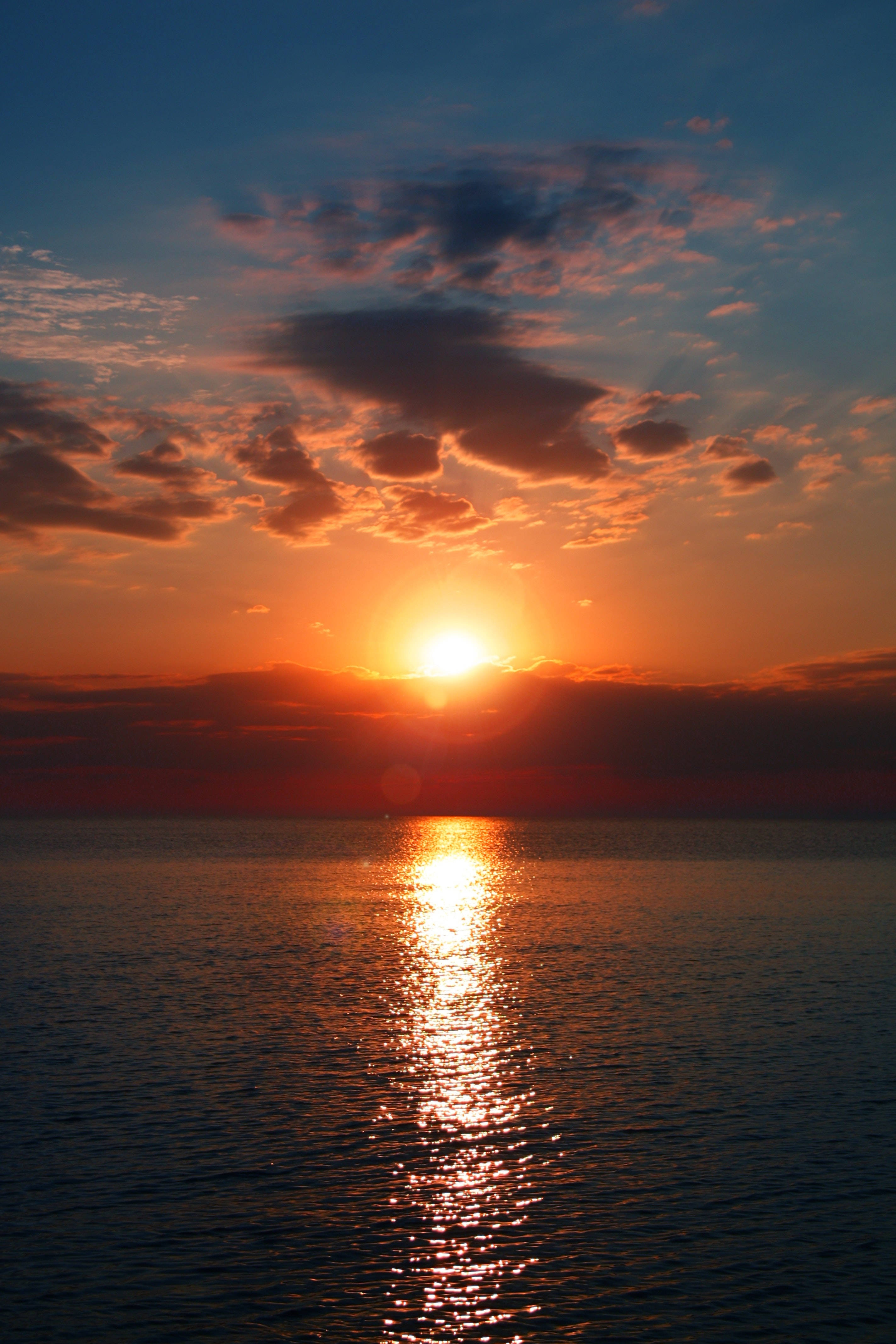 日落雲海的唯美天空 壁紙 — 夕陽將天空染成火熱的橙色和深藍色，太陽在平靜的海面上沉入地平線。