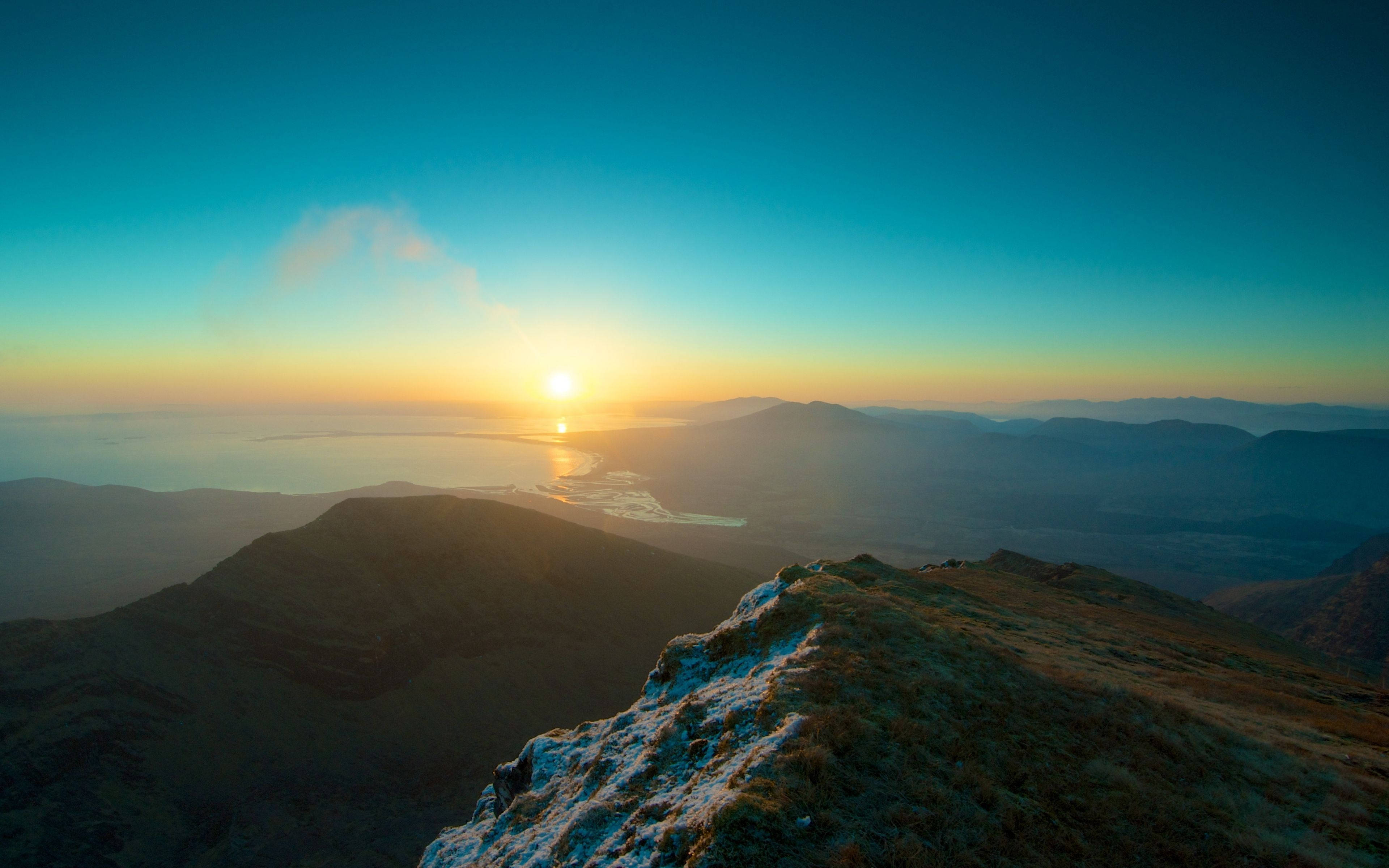 日落風景桌面4K 壁紙 — 日落照亮山脊，遠方山峰和下方平靜的海面。