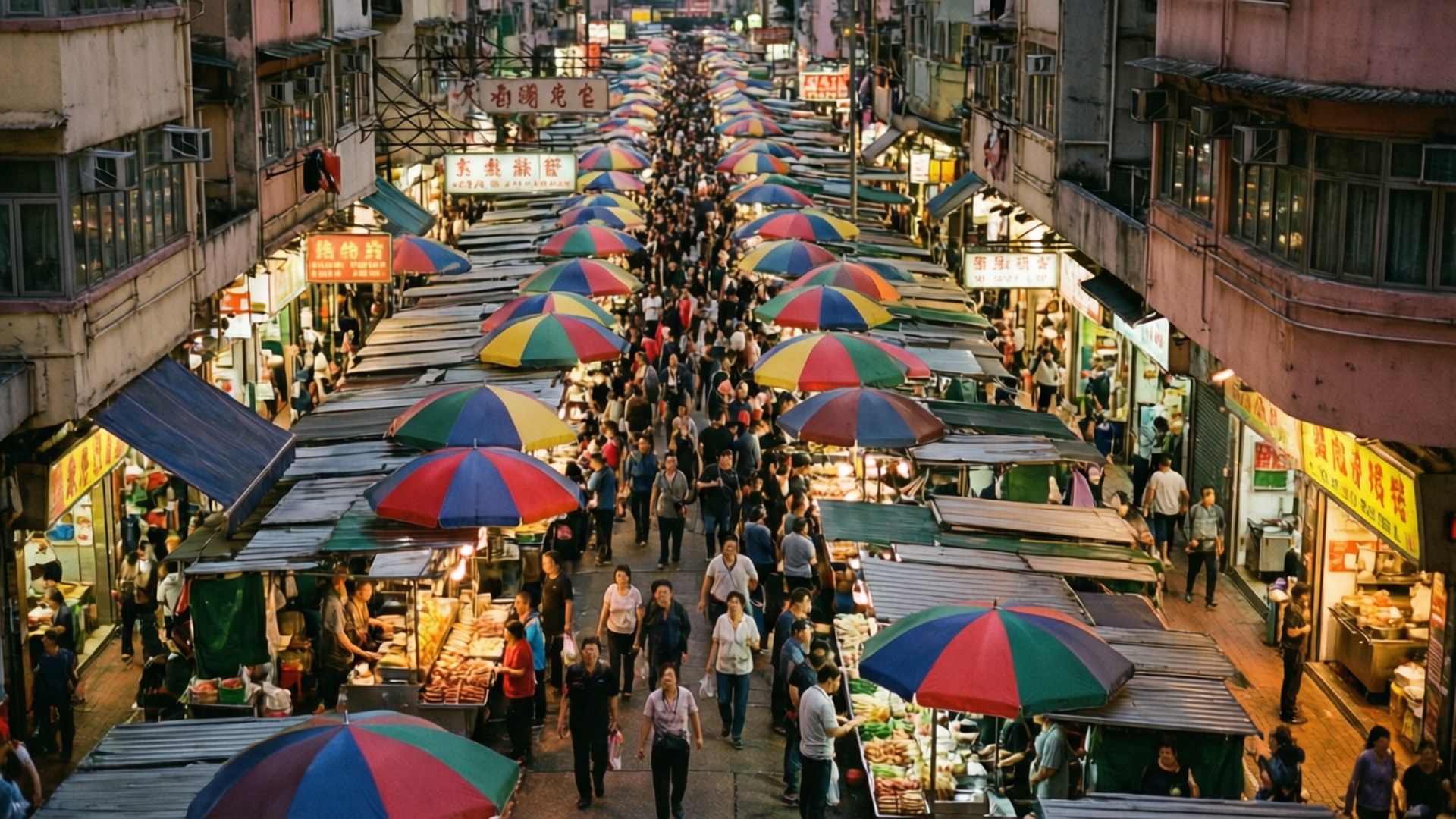 旺角市場混亂景象 壁紙 — 一條熙熙攘攘的夜市街道，擠滿人群，食物攤檔上方掛滿彩色雨傘。