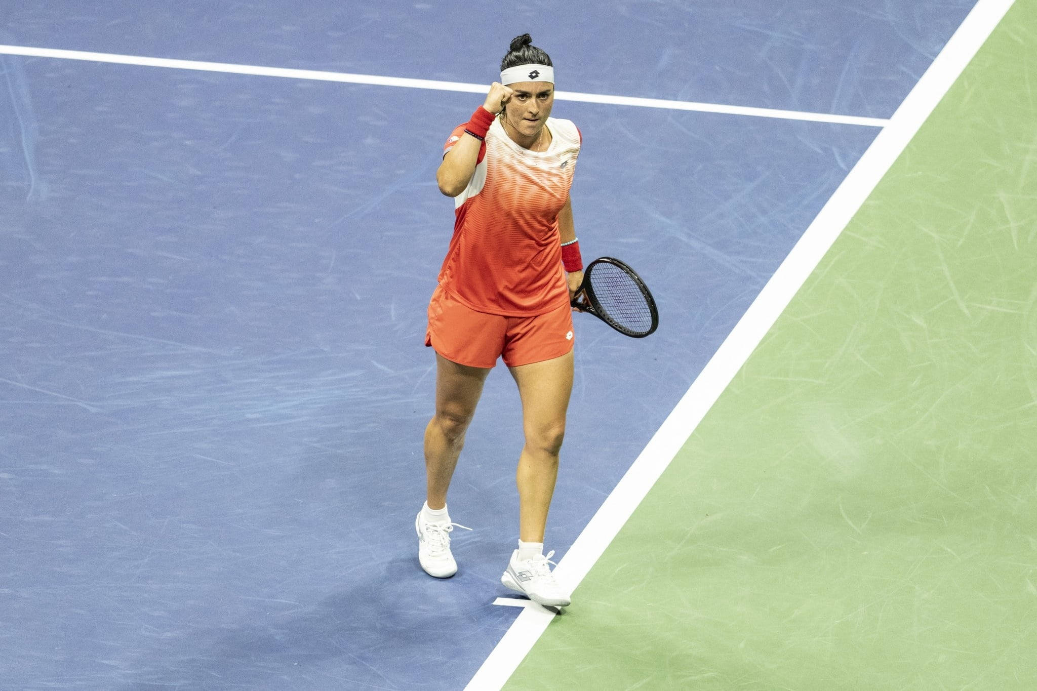 昂斯·賈比爾決心奪勝 壁紙 — 一位身穿橙色裝備的女網球運動員站在藍綠色的球場上，專注地調整頭帶。