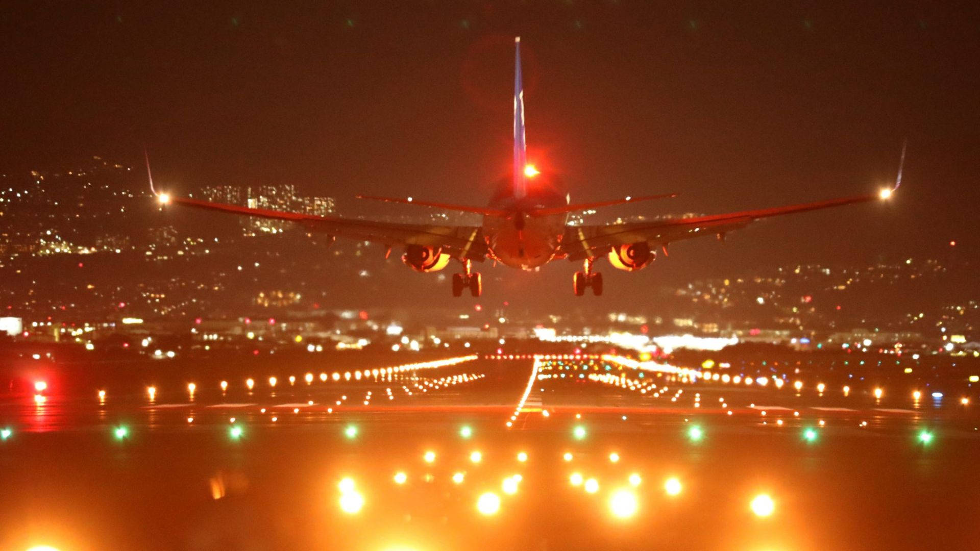 明亮夜間跑道 壁紙 — 一架商用飛機在夜間下降，跑道燈光閃爍，遠處的城市景觀閃爍。