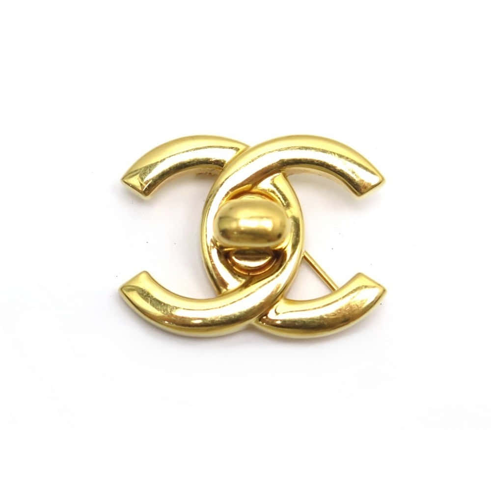 明亮奢華的香奈兒標誌 壁紙 — 閃亮金色Chanel CC標誌胸針，帶有交織的C字和中央珠子，置於純白背景上。