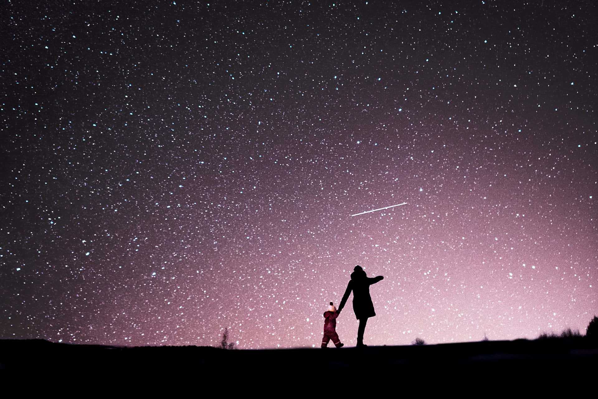 明亮星辰照亮夜空 壁紙 — 一位母親和孩子的剪影手牽手站在廣闊的星空下，一顆流星劃過頭頂。