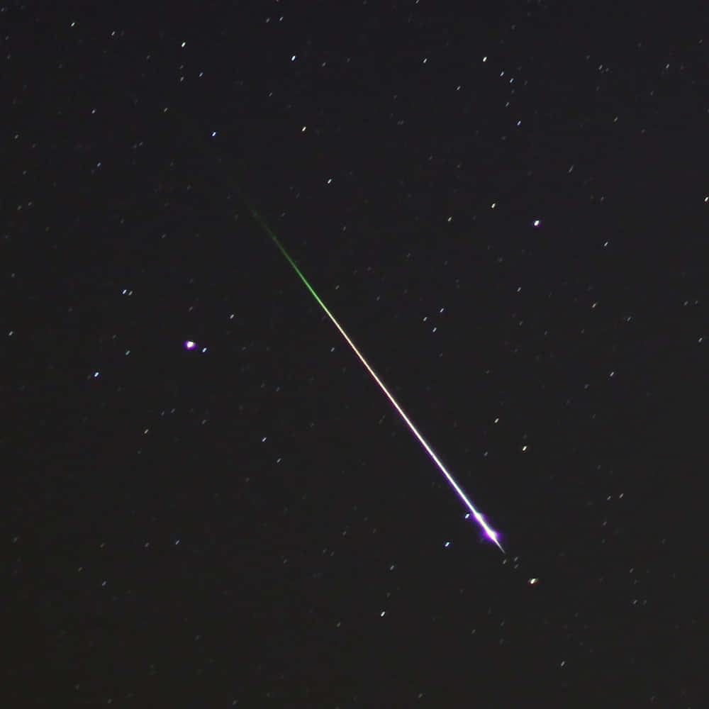 明亮流星劃過深邃夜空 壁紙 — 一顆充滿活力的流星斜斜地劃過繁星點點的夜空，留下一條發光的綠色和紫色痕跡。