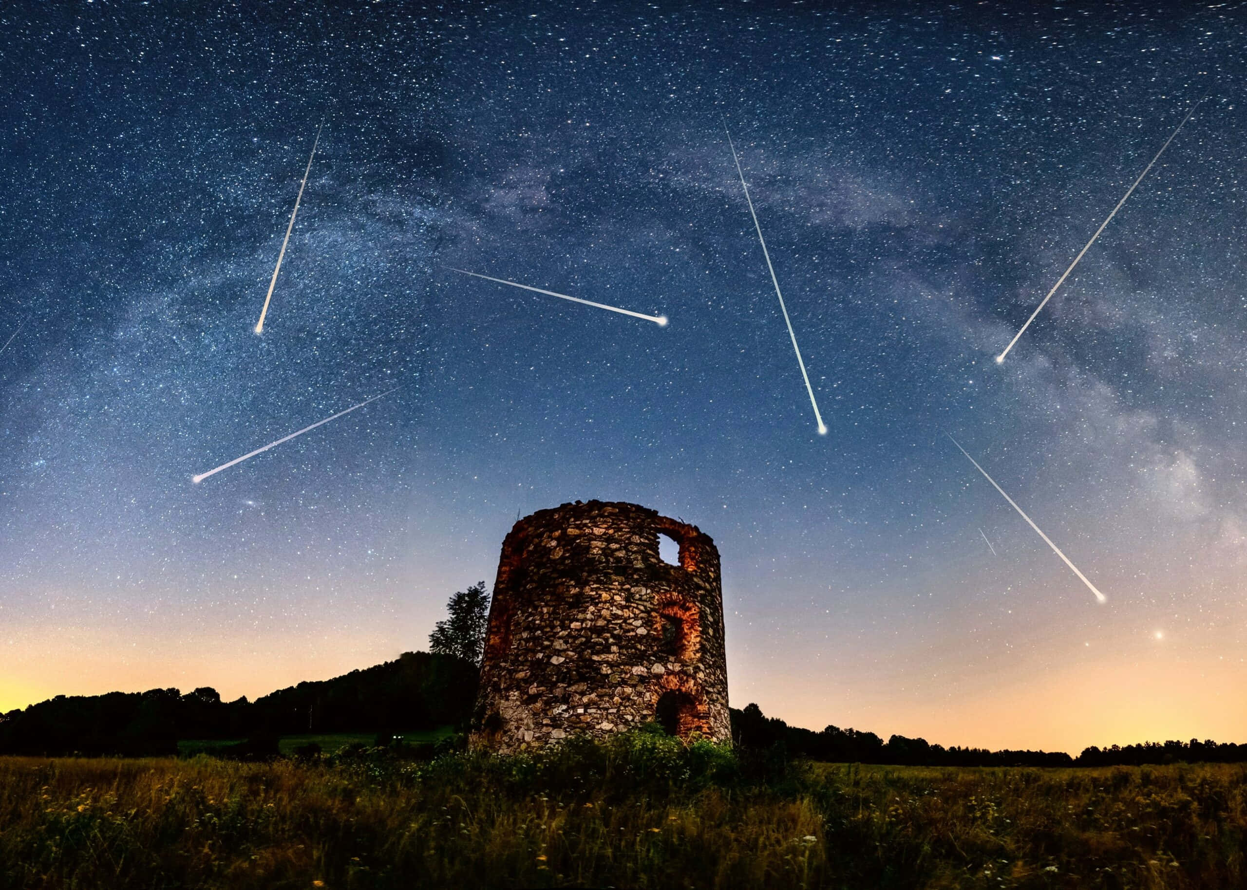 明亮的流星劃過夜空 壁紙 — 古老的石塔矗立在田野中，上方是劃過流星和銀河光芒的星空。