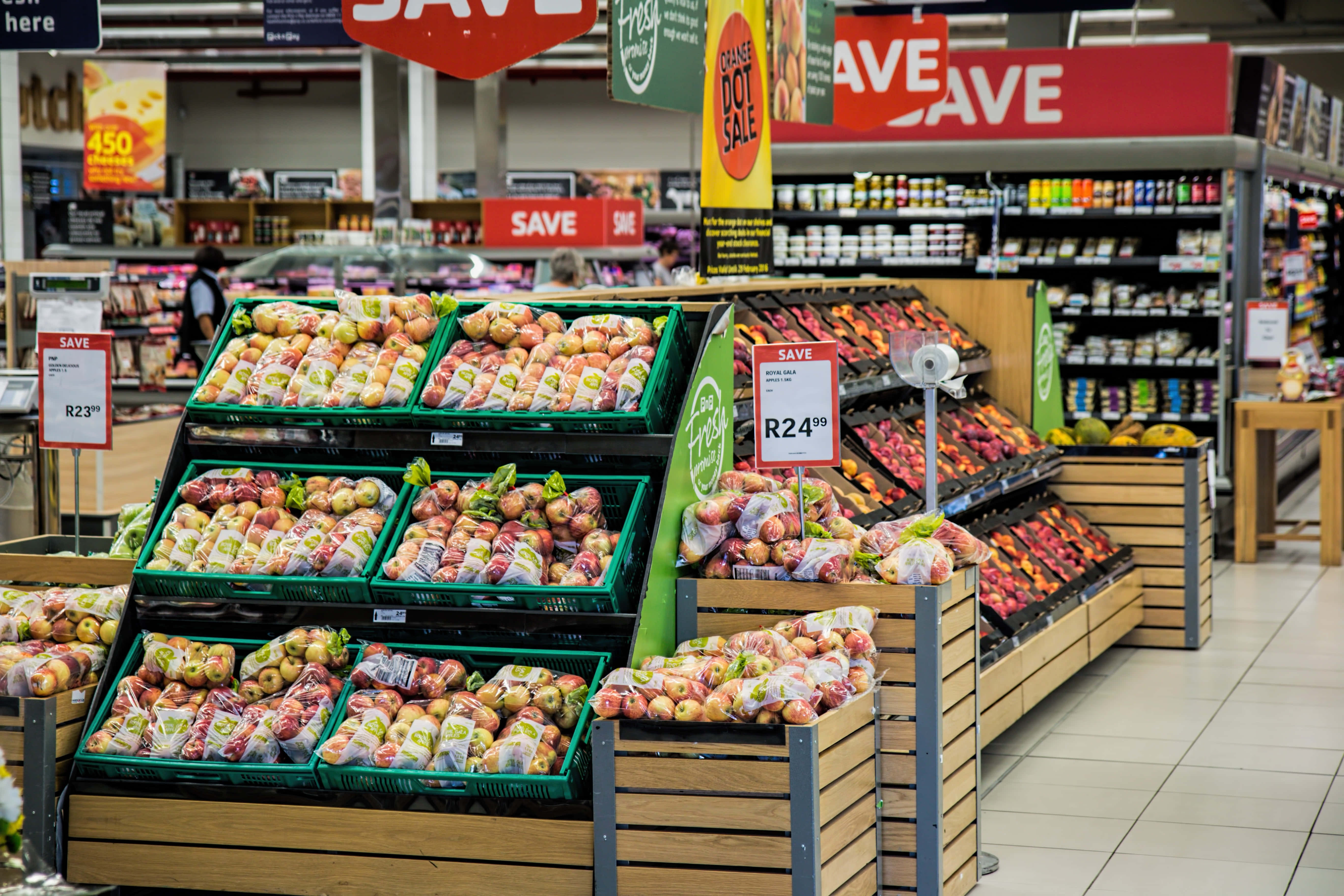 Grocery Store 桌布 壁紙 — 明亮的超市通道，綠色板條箱裡裝滿了色彩繽紛的蘋果，上方掛著「SAVE」促銷標誌。