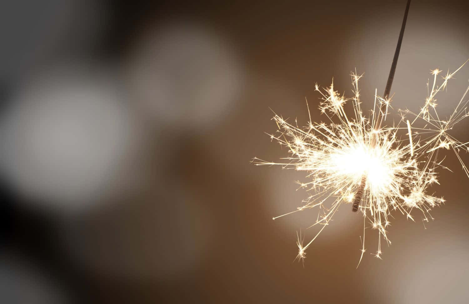 一個點燃的煙花棒在模糊的背景上發出明亮的金色火花。 — 新年動畫 壁紙