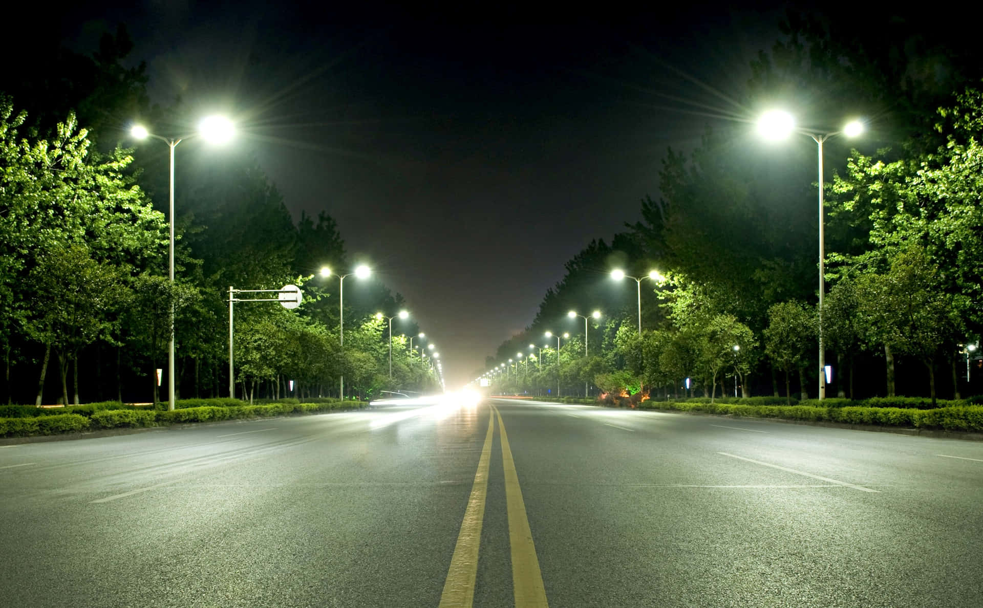 夜晚一條寧靜空蕩的道路，被路燈照亮，兩旁有樹木。