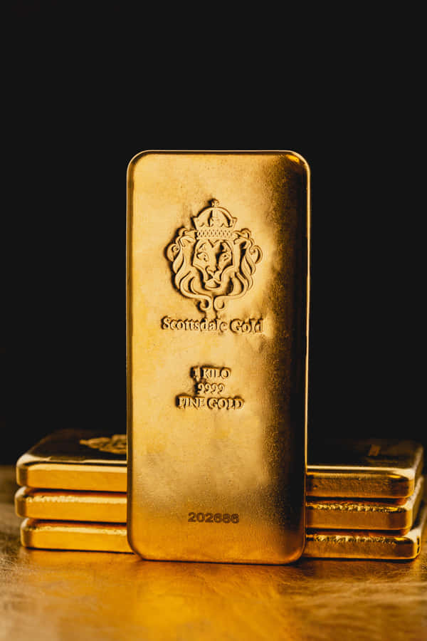 明亮閃耀的金屬背景 壁紙 — 一塊閃閃發光的一公斤金條，帶有獅子徽章，直立於黑色背景前，兩側堆疊著類似的金條，置於反光的金色表面上。