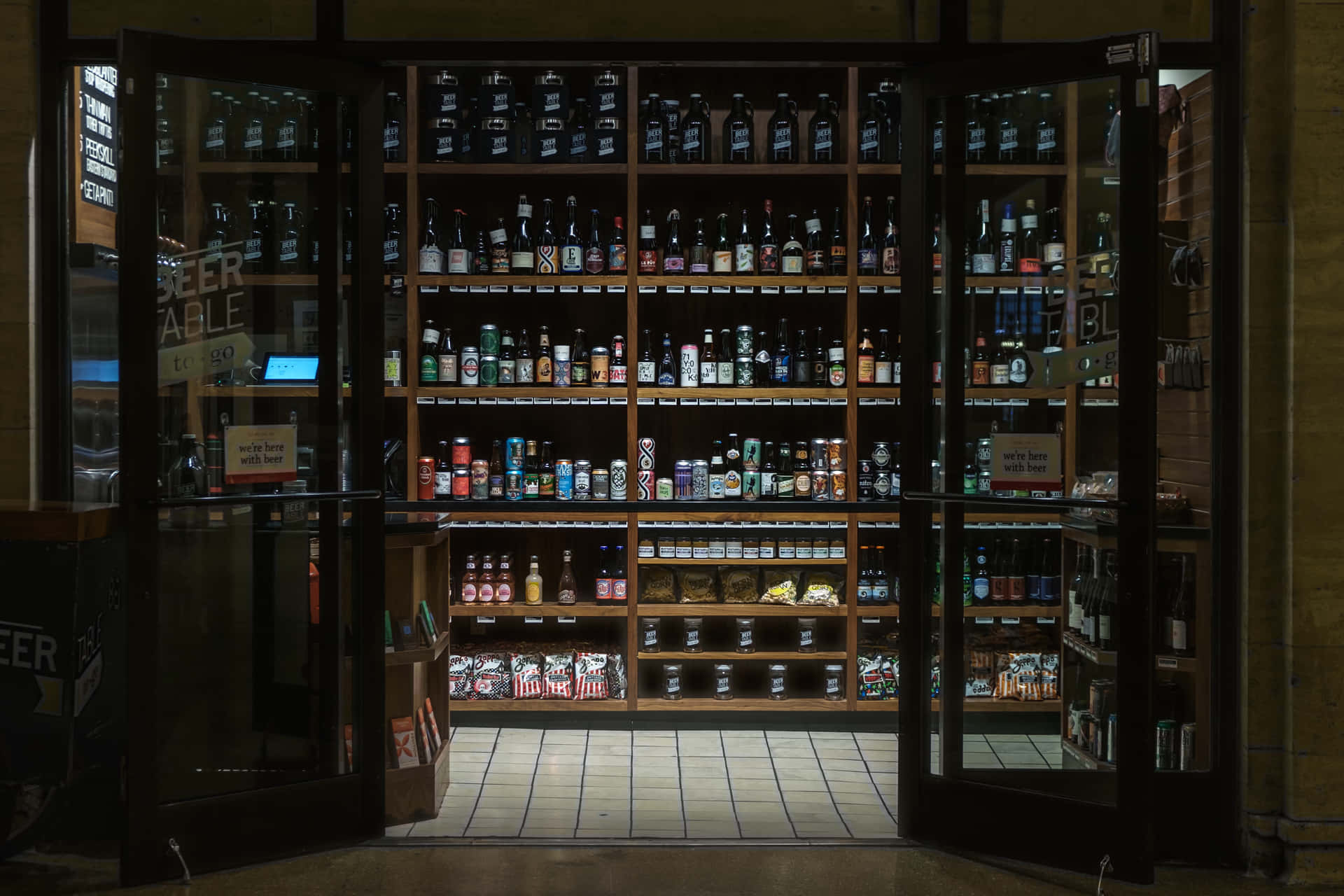 打開的玻璃門揭示了一家啤酒商店，裡面有裝滿瓶子和罐子的貨架。