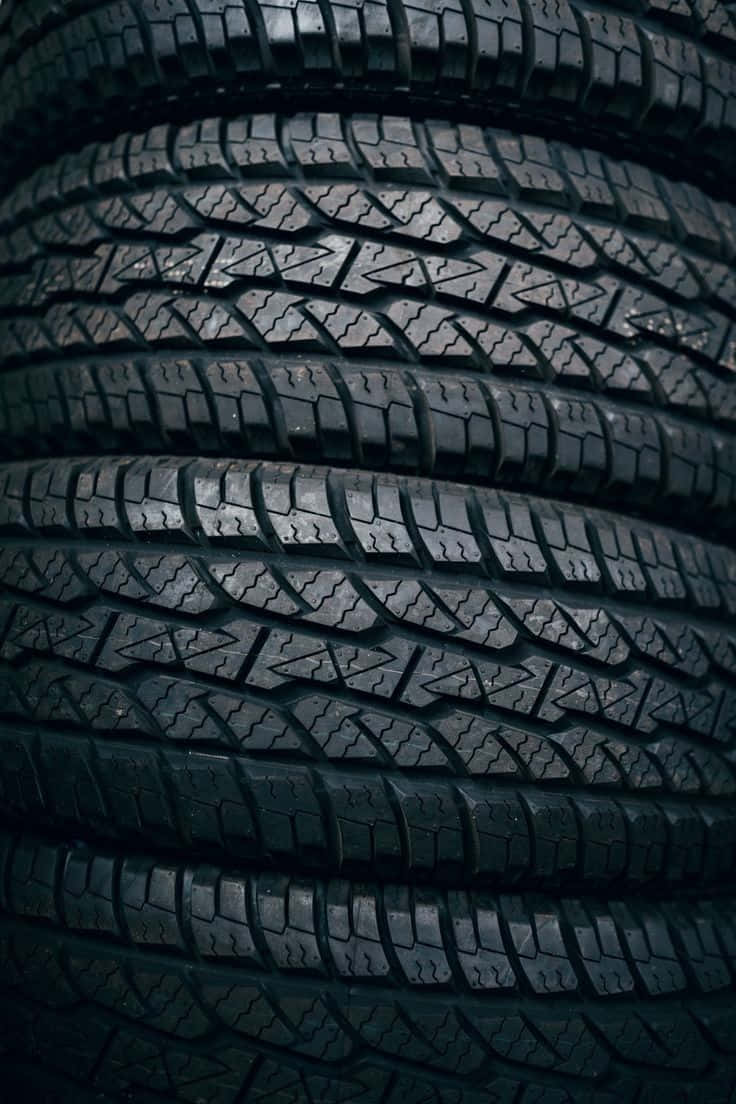 Winter Tires 桌布 壁紙 — 昏暗燈光下堆疊黑色橡膠輪胎的特寫，顯示詳細的胎面花紋。