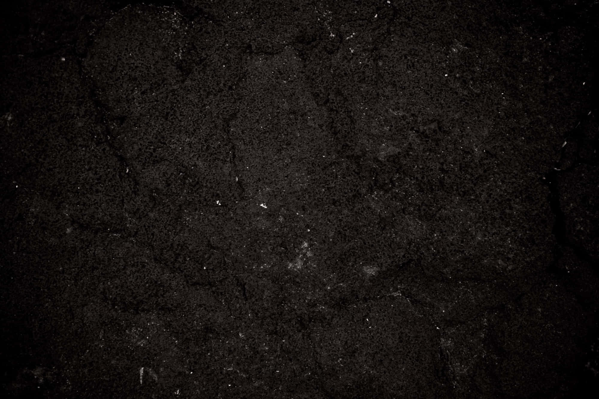 Dark Rock 桌布 壁紙 — 昏暗燈光下粗糙深色龜裂泥土的特寫，帶有細微白色斑點。