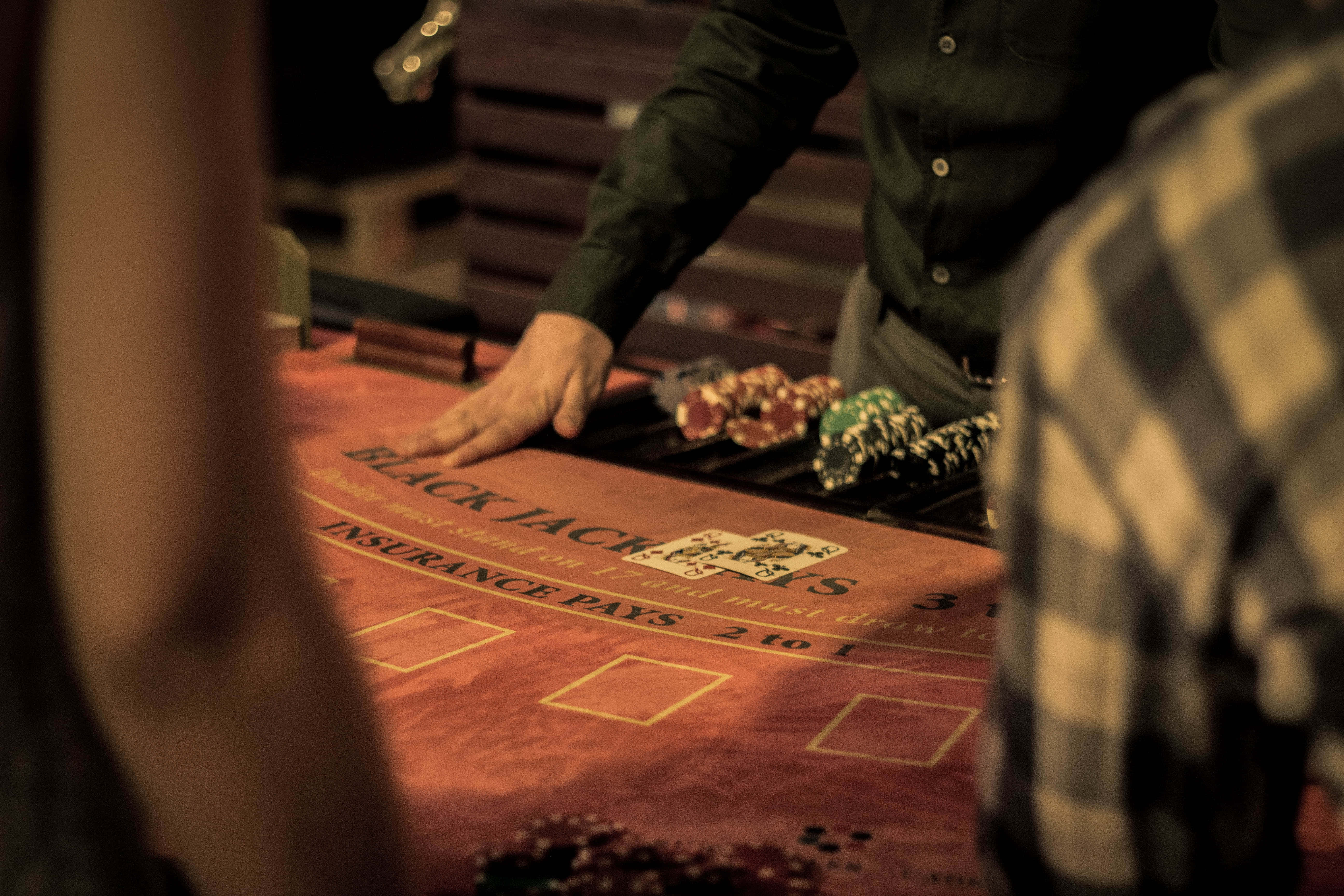 Poker Table 桌布 壁紙 — 昏暗賭場中廿一點賭枱的特寫，莊家的手放在一堆彩色籌碼旁邊。