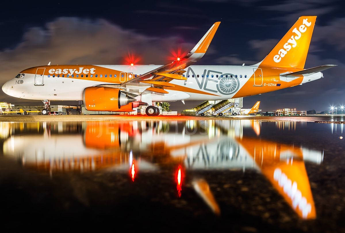 橙色和白色的易捷航空飛機夜間停放，在濕滑跑道上反射。
