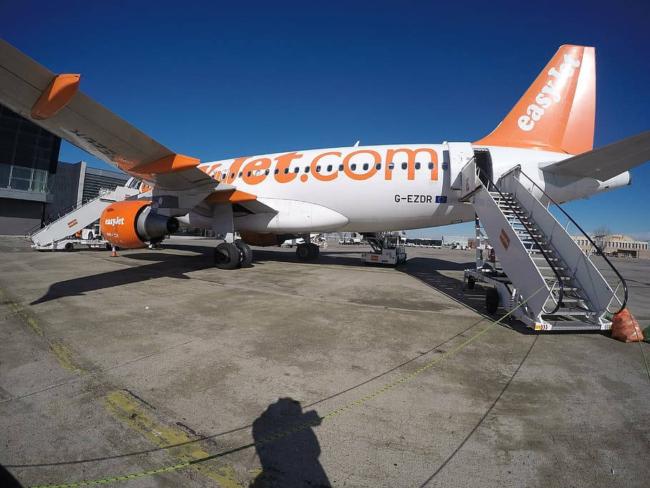 易捷航空飛機停在機場閘口，附有登機梯和晴朗藍天。