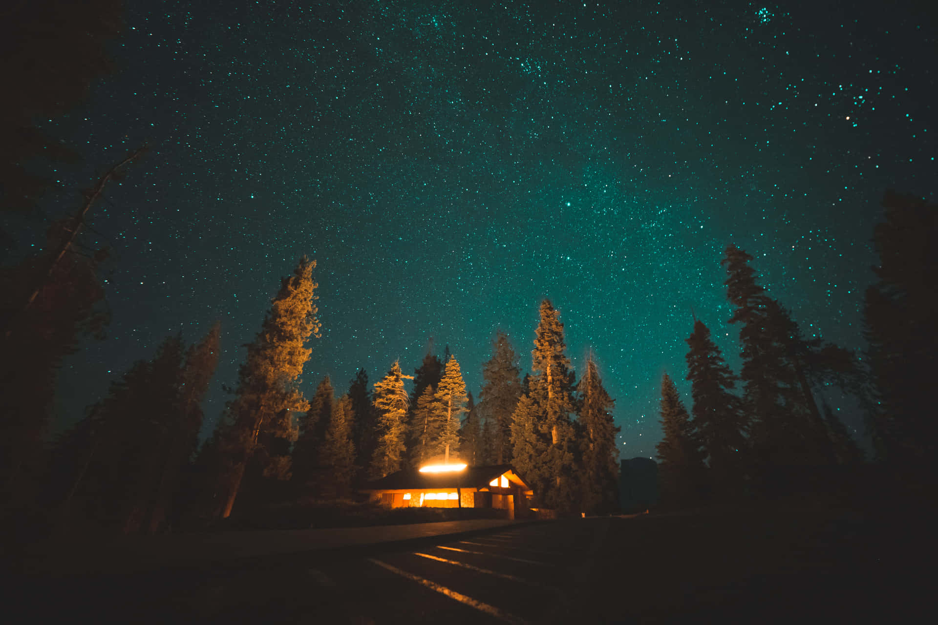 一間溫暖照明的小屋，被松樹環繞，上方是星空。