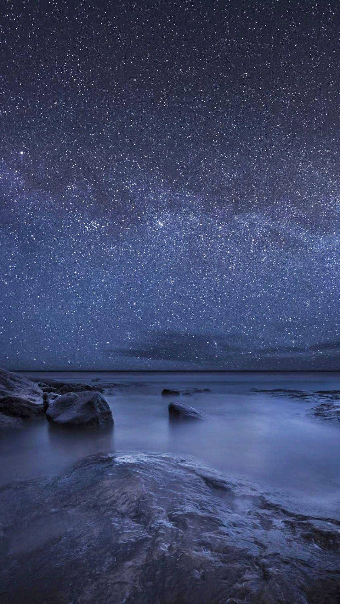 平靜海洋上的星空夜空，光滑流動的水和暗色岩石。