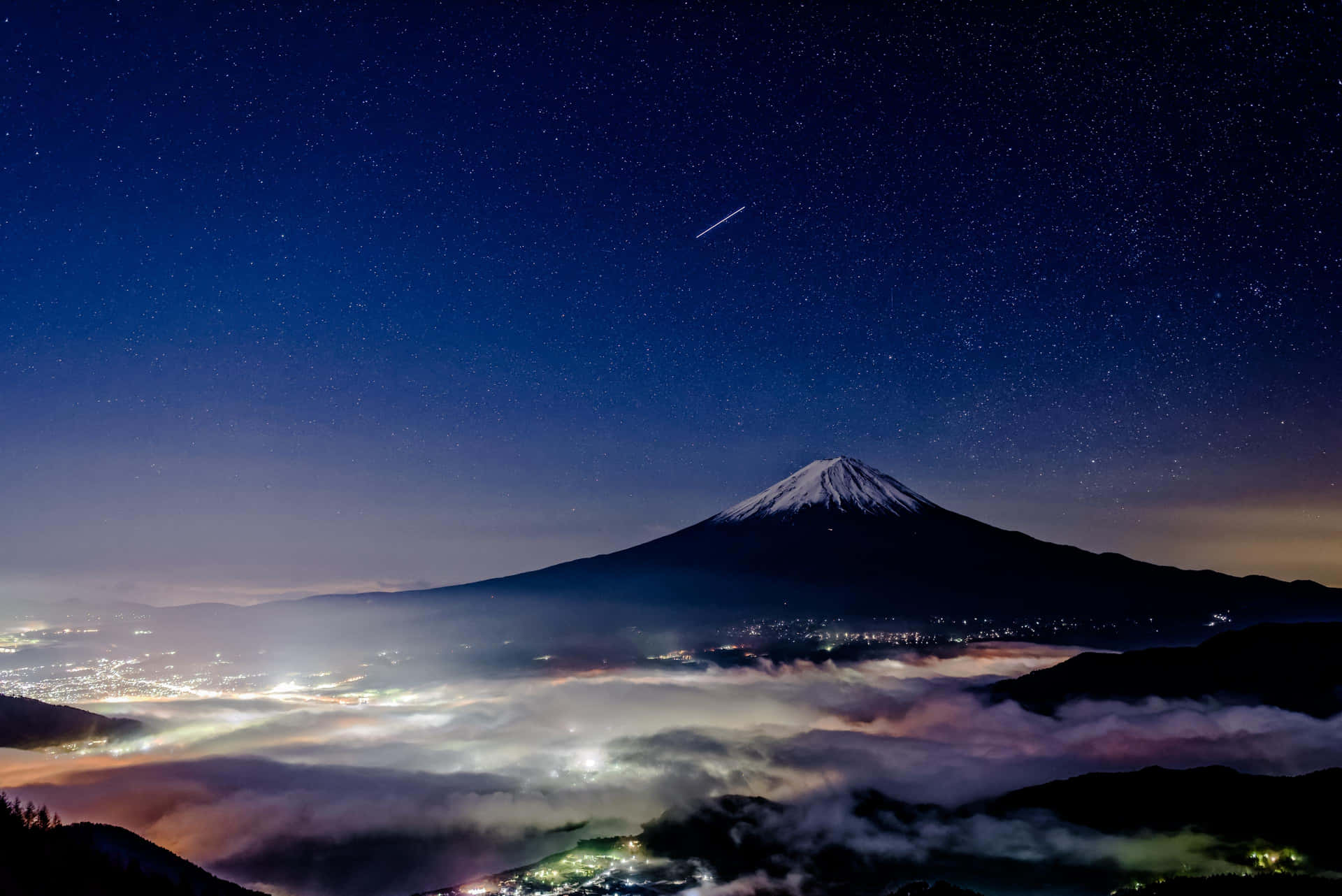 富士山在星空下，下方有發光的雲和城市燈光
