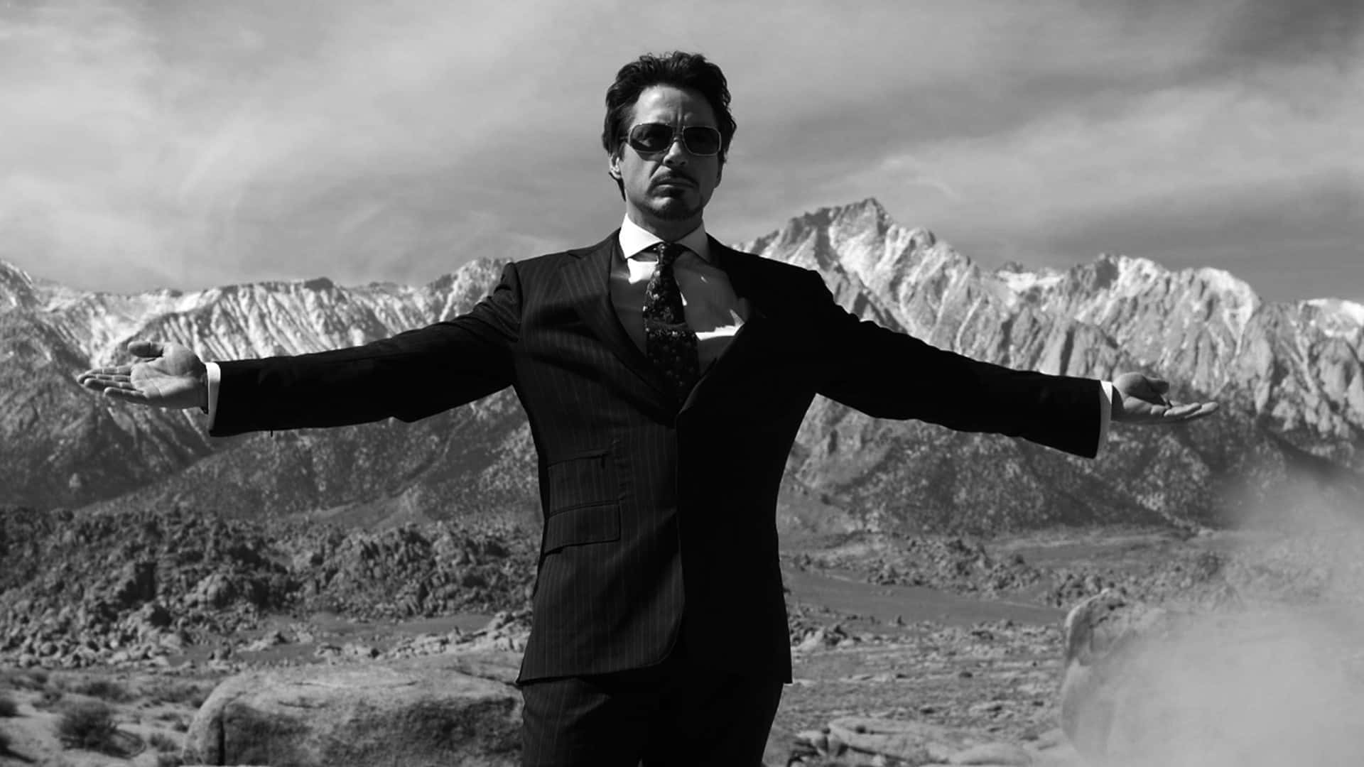 穿著西裝和太陽眼鏡的男人在沙漠山景中張開雙臂站立。