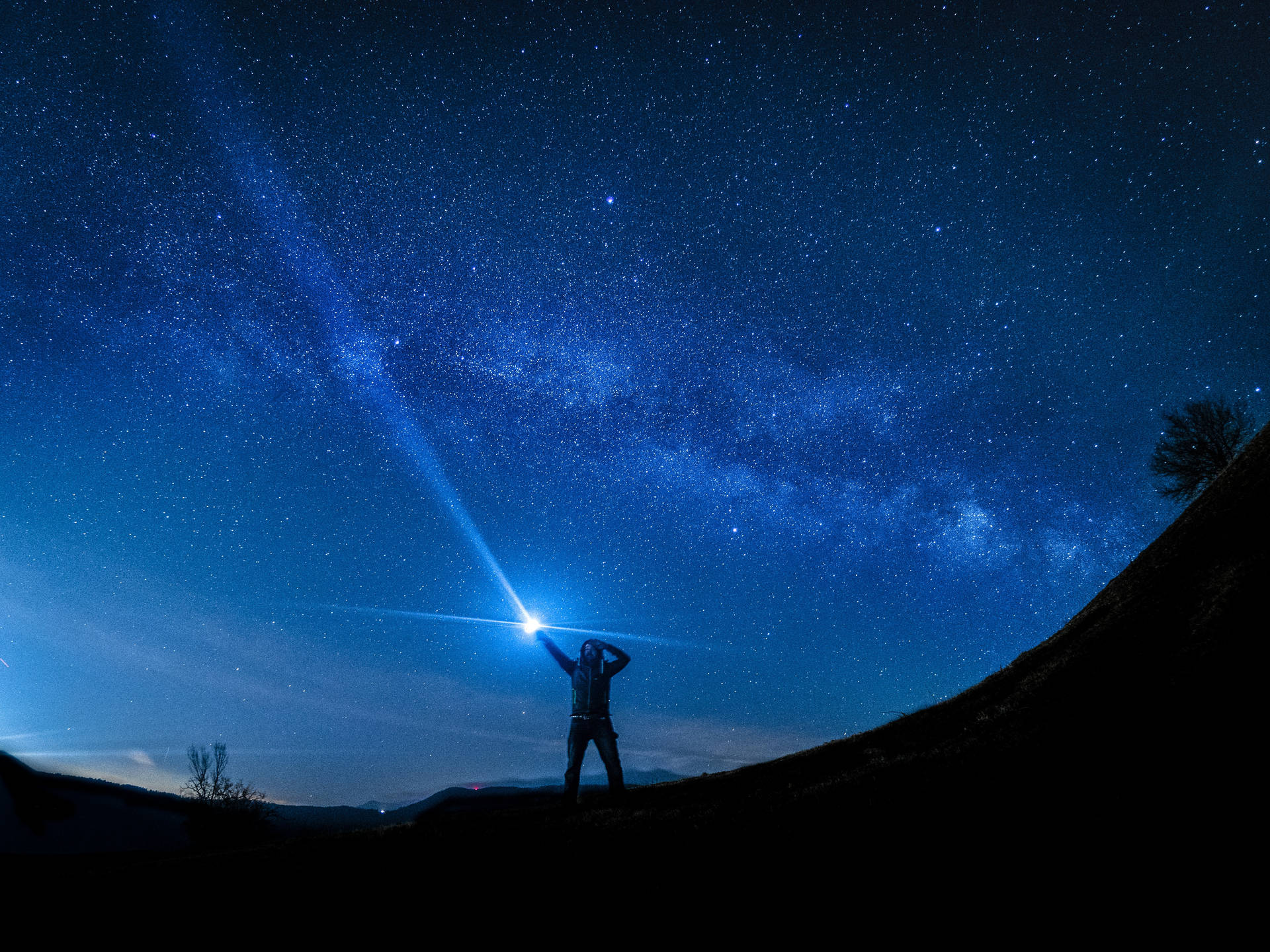 山丘上的人將手電筒指向可見銀河系的星空