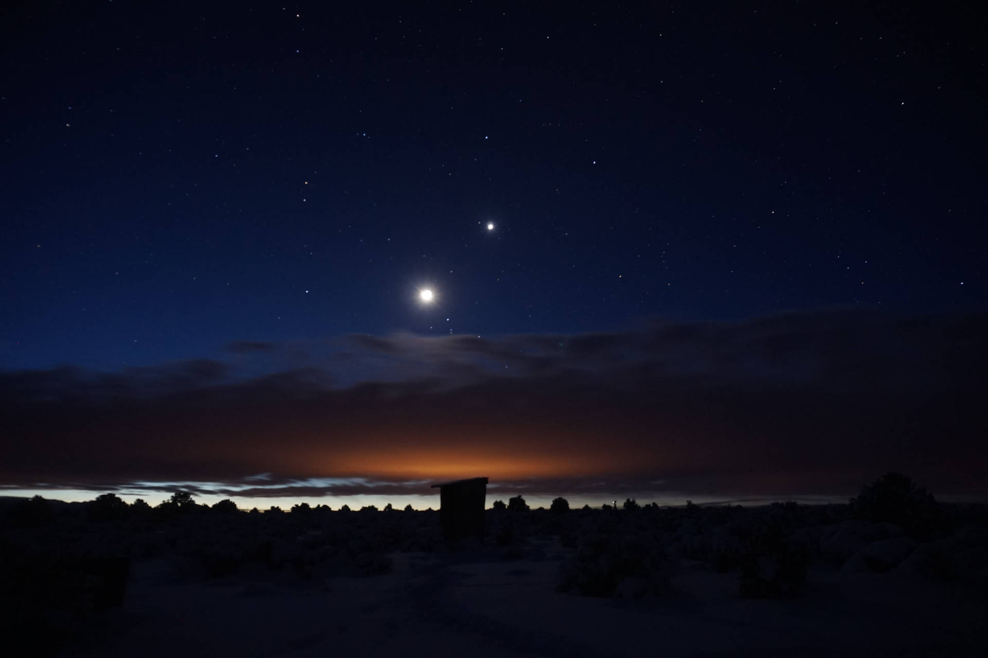 夜晚的雪沙漠景觀，有星星、月亮和橙色地平線光芒。