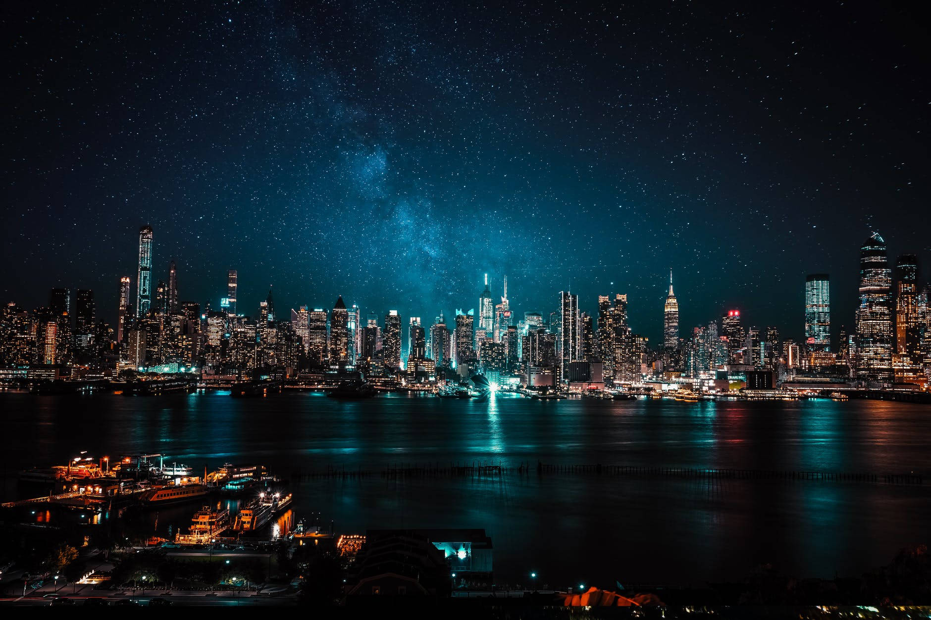 星夜摩天大樓城市 壁紙 — 在星空下，閃爍的摩天大樓和反射的水面上方，銀河拱橋橫跨的紐約天際線夜景，令人目眩神迷。
