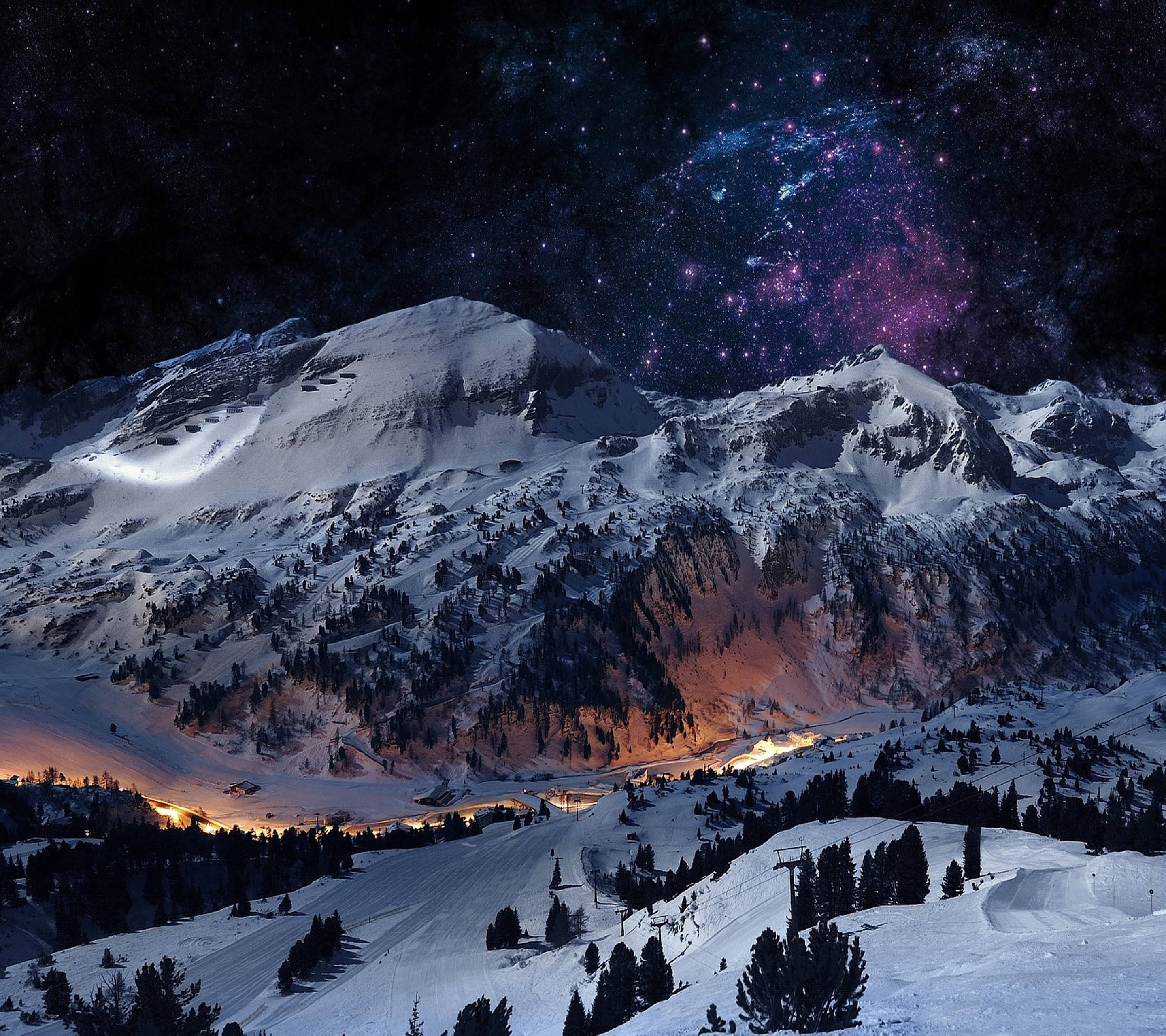 星夜溫馨冬日 壁紙 — 白雪覆蓋的山峰，在充滿活力的紫色和藍色星空下，下方有發光的山谷燈光。