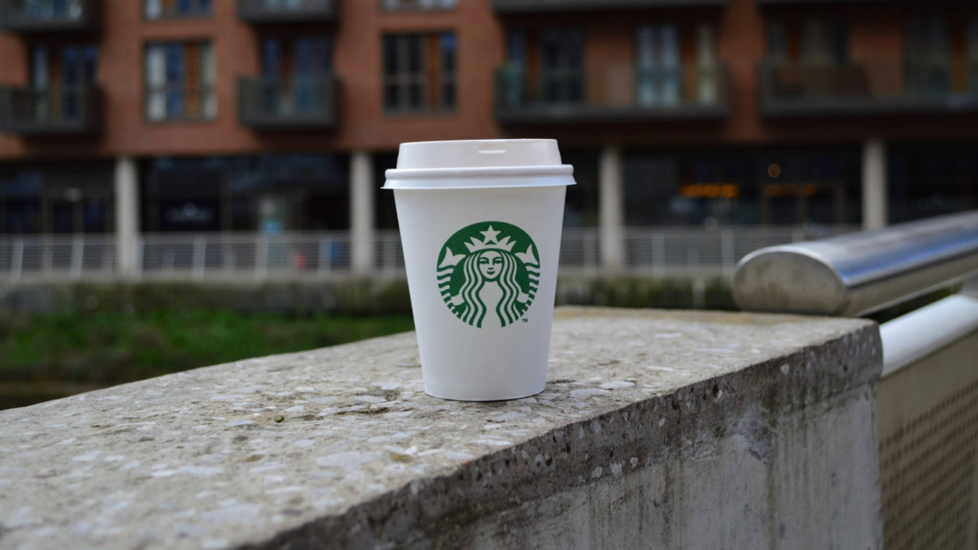 一個Starbucks咖啡杯放在混凝土欄杆上，背景是城市建築。