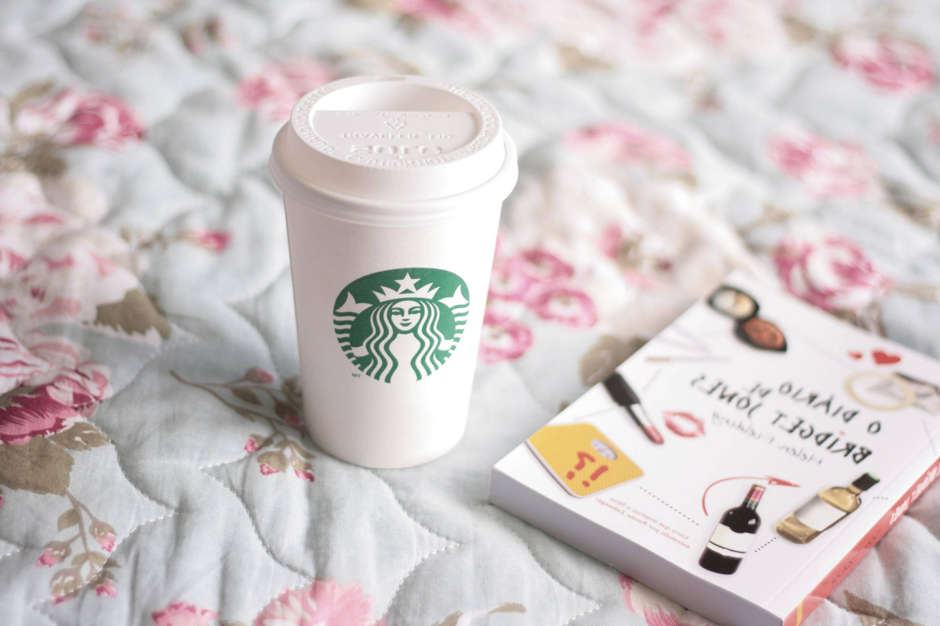 Starbucks咖啡杯和書放在花卉絎縫床罩上。