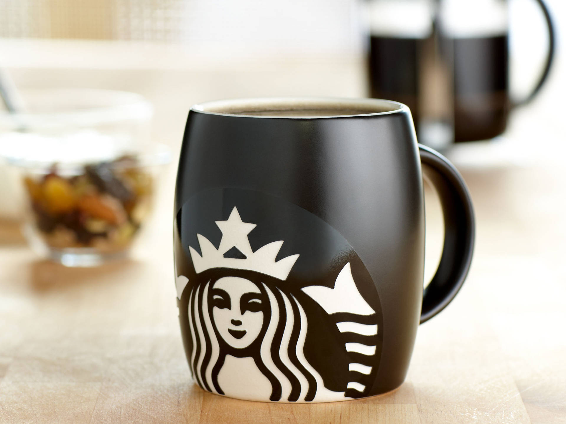 木桌上的黑色Starbucks咖啡杯，背景有雜錦堅果和咖啡壺。