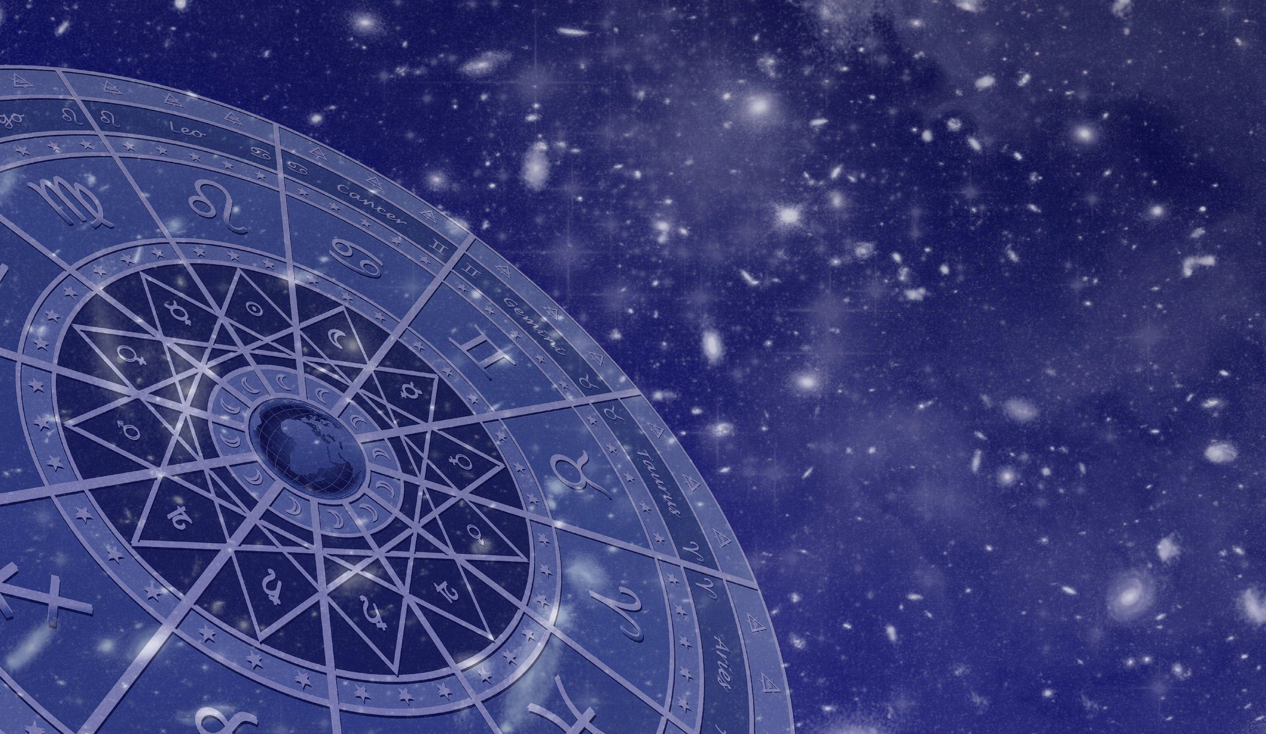 星座星盤銀河圖 壁紙 — 一個發光的占星輪盤，帶有星座符號，漂浮在星光閃爍的宇宙藍色背景上。