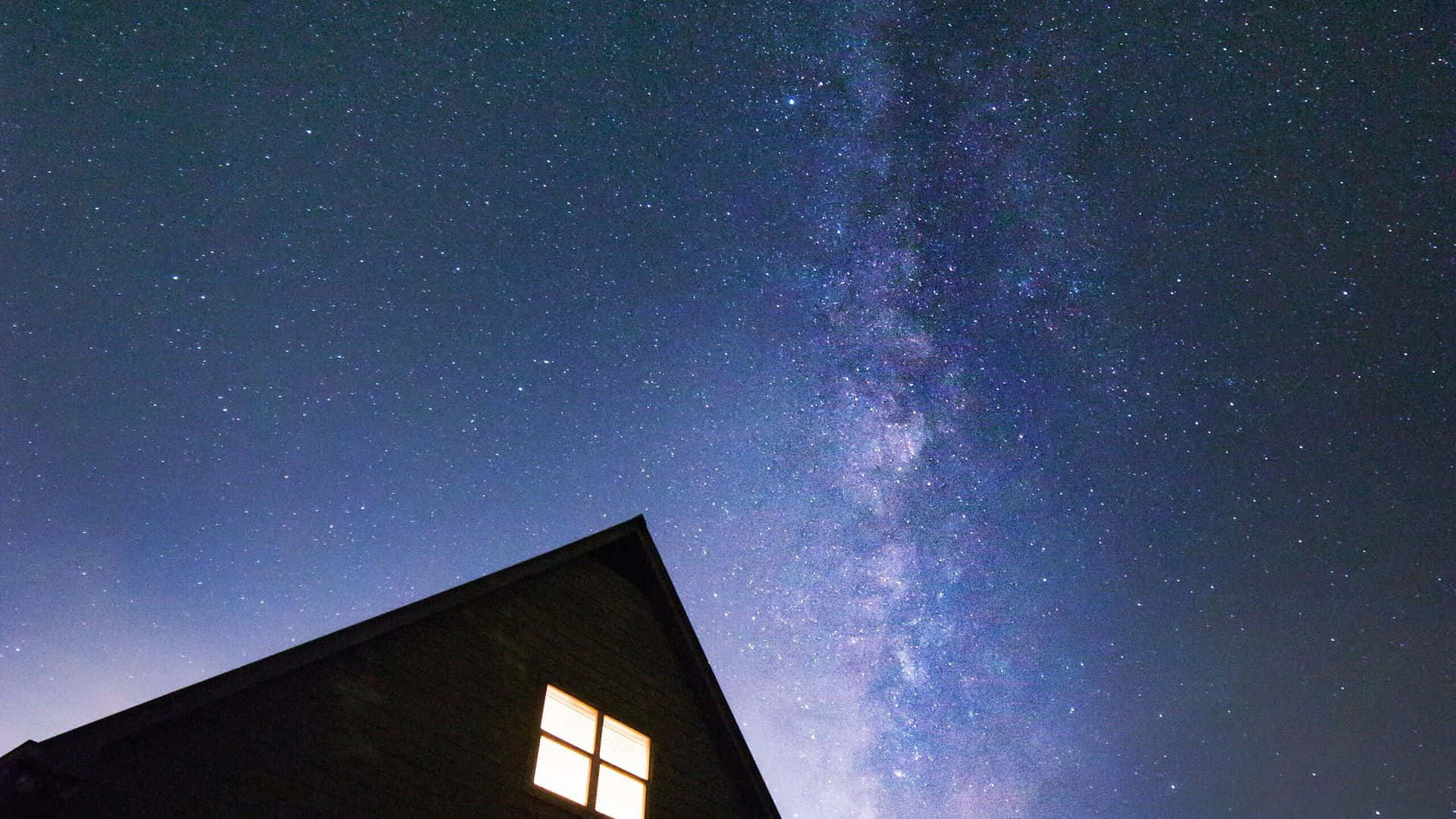 在可見銀河系的星空下發光的房屋窗戶。