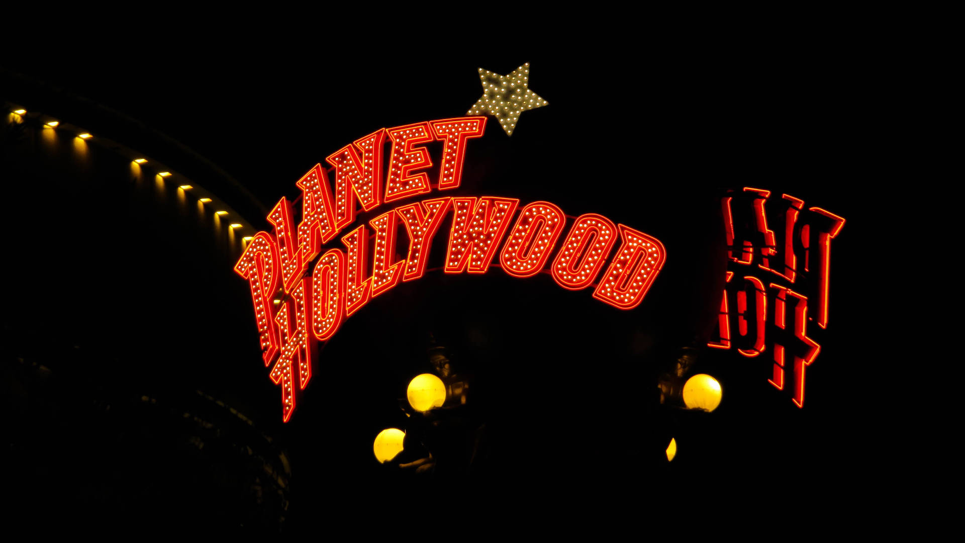 星球好萊塢招牌 壁紙 — 一個鮮紅色的霓虹招牌寫著「Planet Hollywood」，在漆黑的夜空下閃耀，上方有一顆星星，下方有溫暖的燈光。